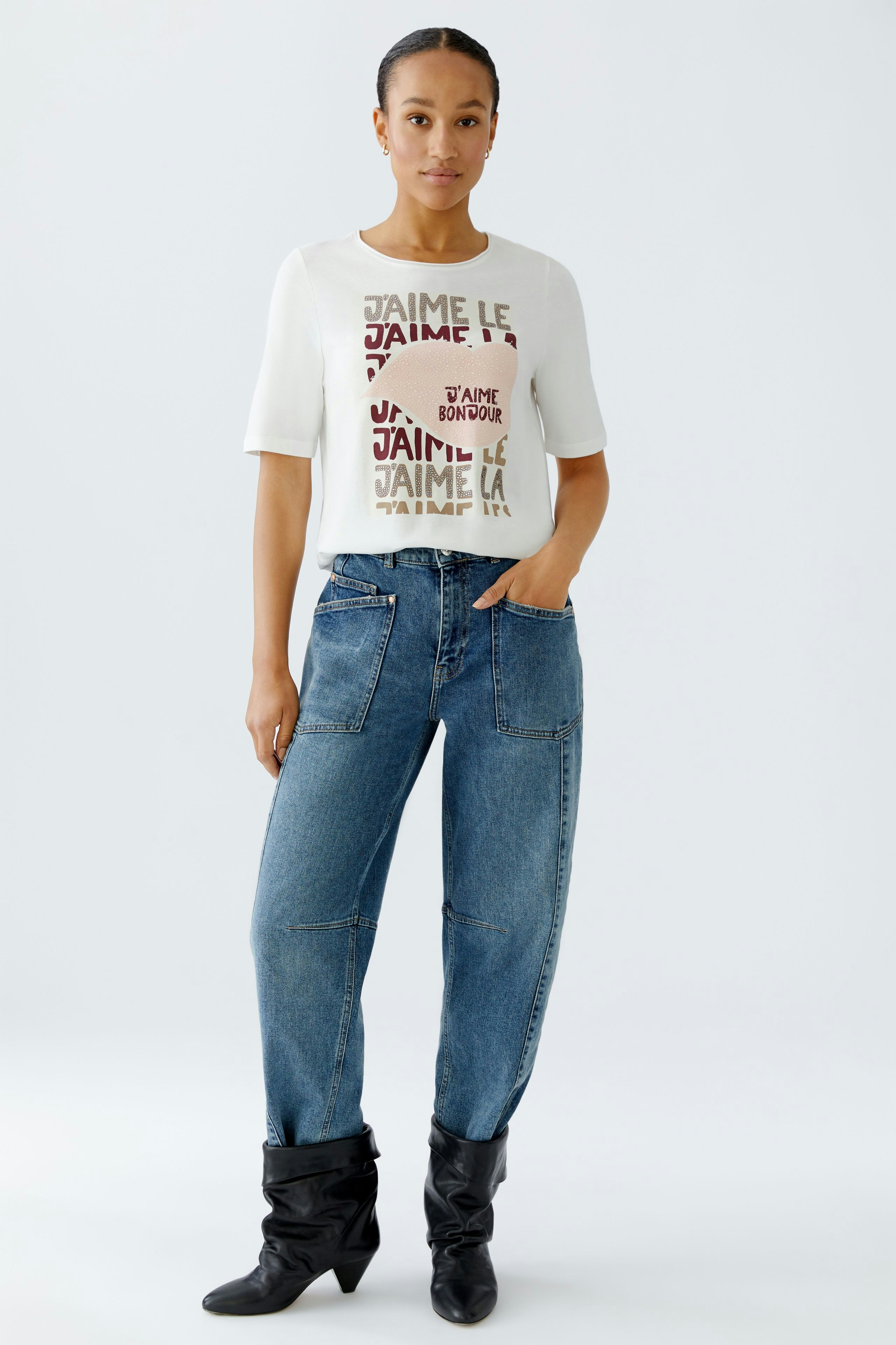 Casual women's T-shirt: Woman in a white tee with colorful text and relaxed-fit jeans.