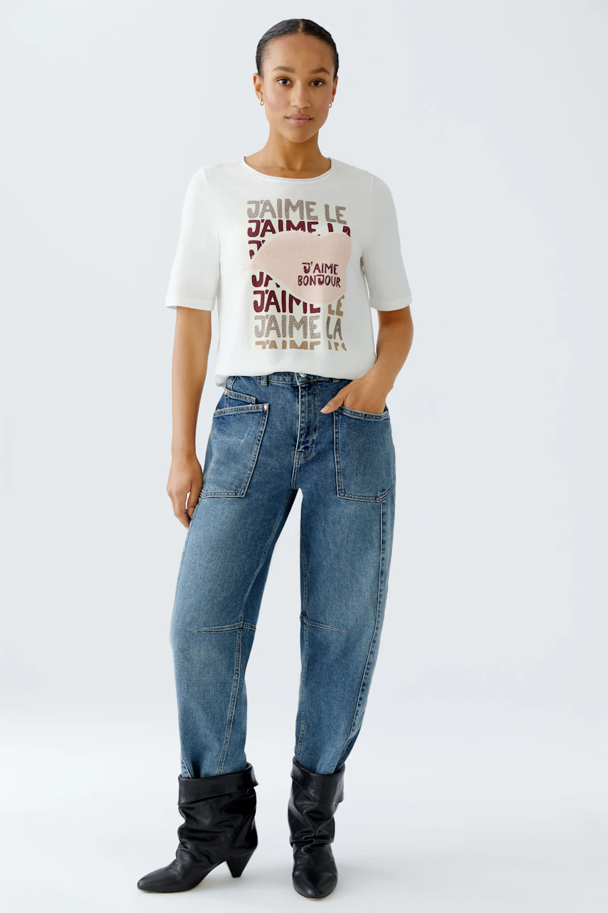 Casual women's T-shirt: Woman in a white tee with colorful text and relaxed-fit jeans.