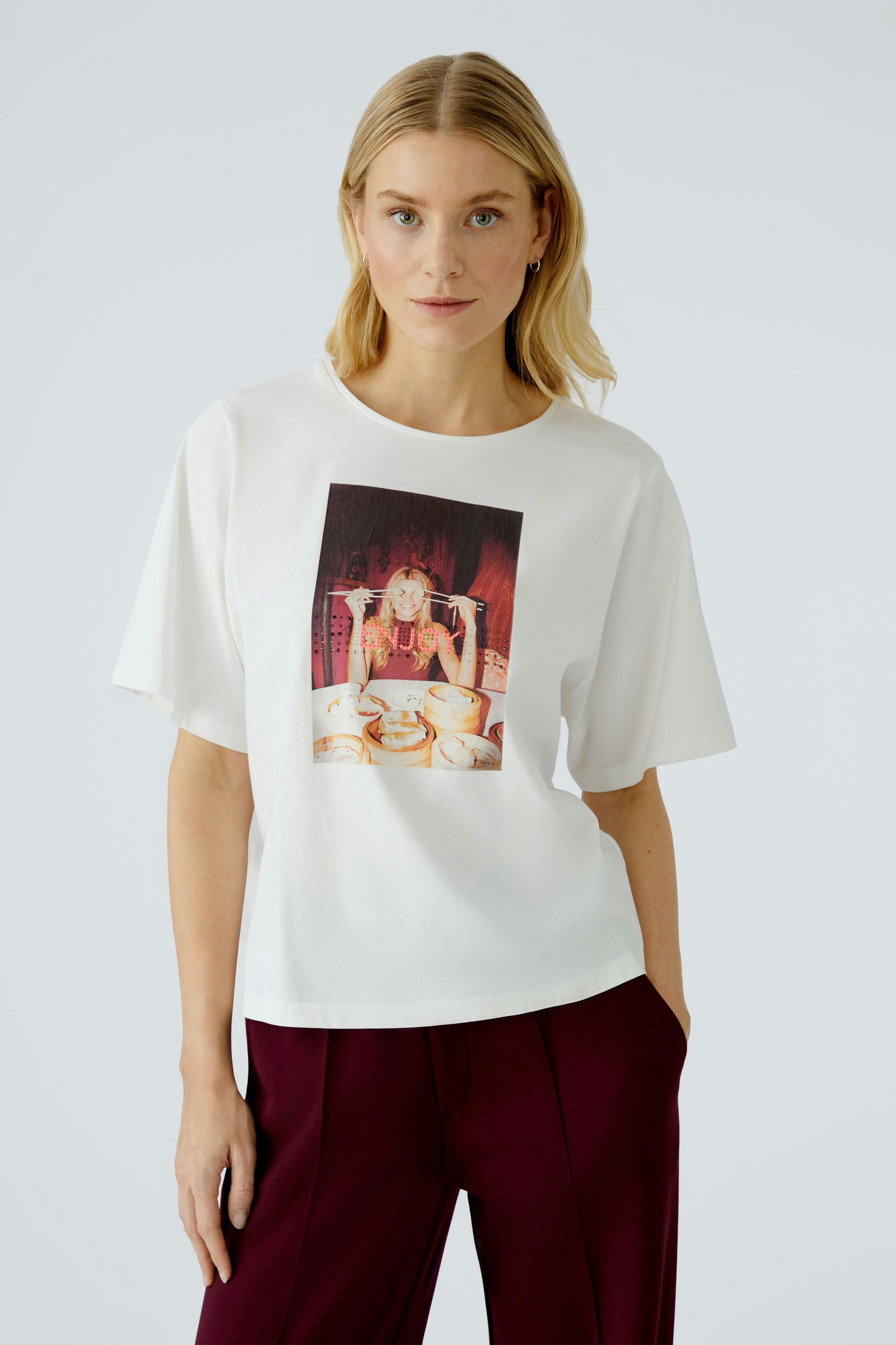 Damen-T-Shirt: Frau in weißem Shirt mit buntem Druck, lässig kombiniert mit weiten Hosen.