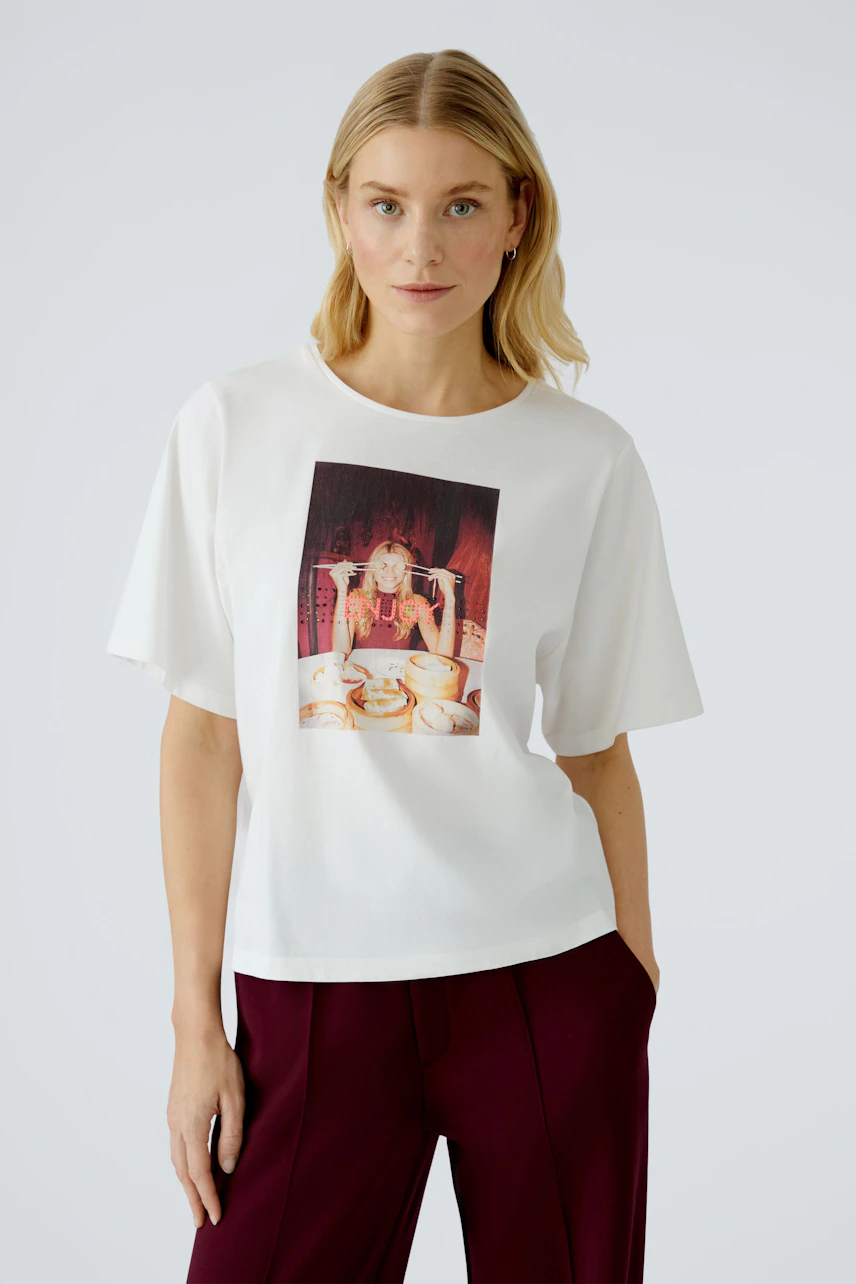 Damen-T-Shirt: Frau in weißem Shirt mit buntem Druck, lässig kombiniert mit weiten Hosen.