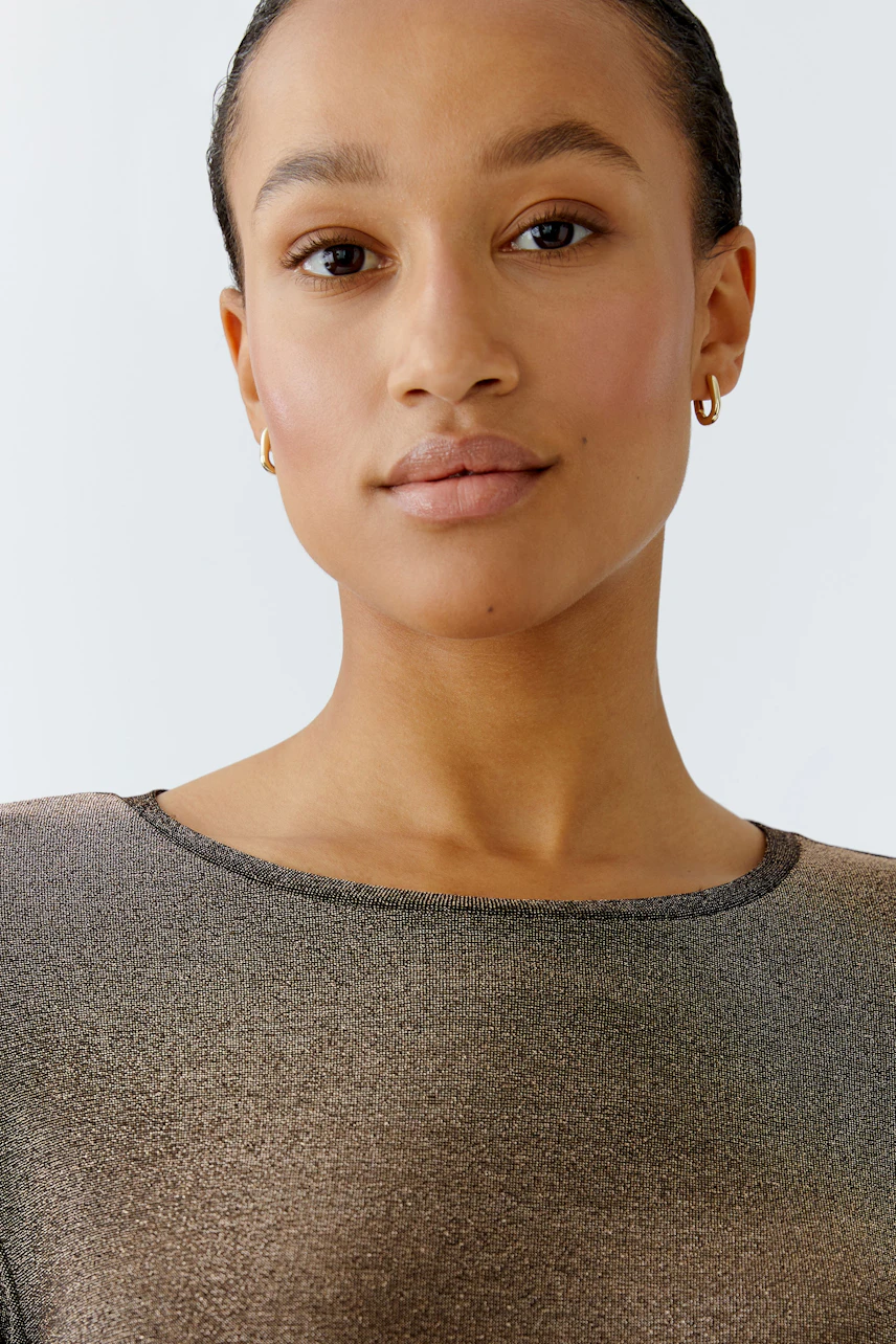 Modern long-sleeve shirt: Woman in a shimmering top with a round neckline, showcasing a casual style.