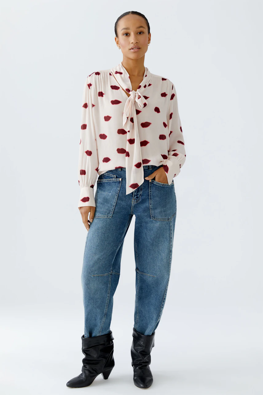 Stylish women's blouse with a tie detail and playful red lips pattern, paired with relaxed jeans.