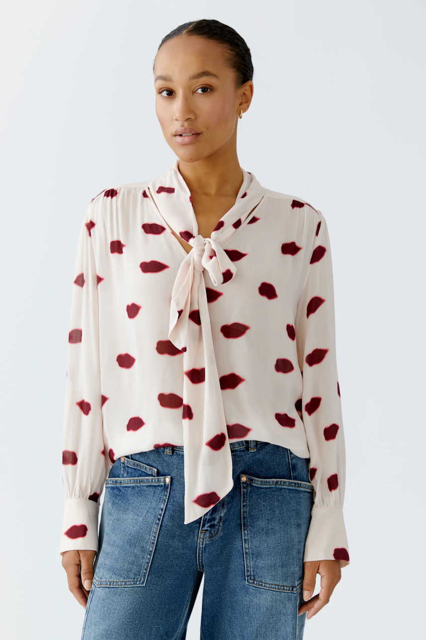 Lightweight blouse: Woman in a cream blouse with red spots and a tie detail, paired with casual jeans.