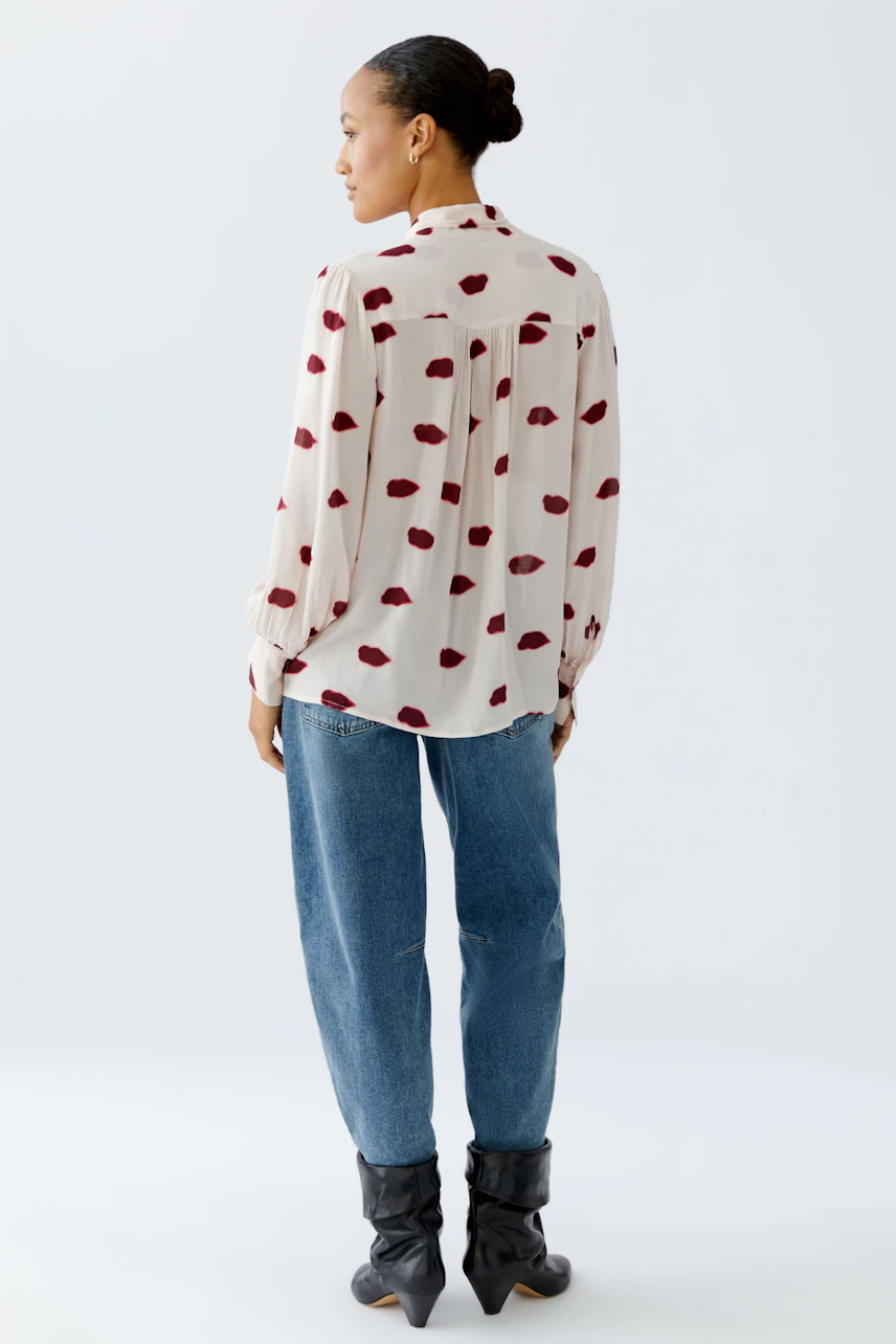 Light blouse with a playful red pattern, worn by a woman, paired with relaxed jeans.