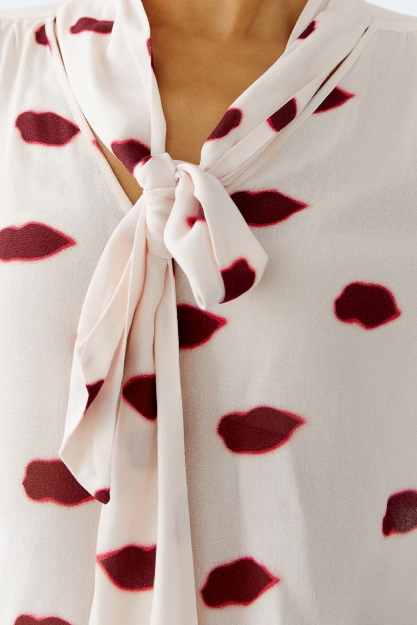 Light blouse with a tie detail, featuring a playful lip print, worn by a woman.