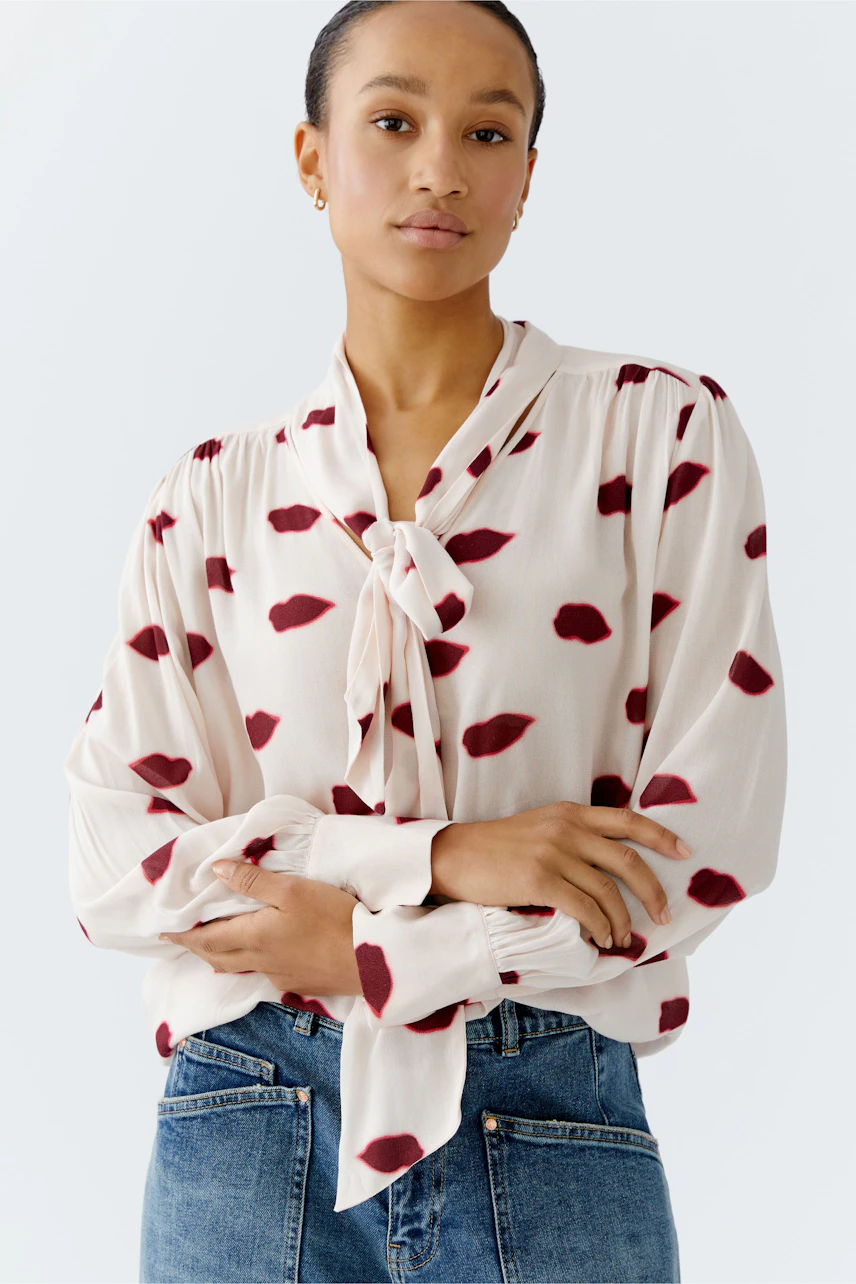 Lightweight blouse with a tie detail, featuring a woman wearing a cream fabric with red spots.