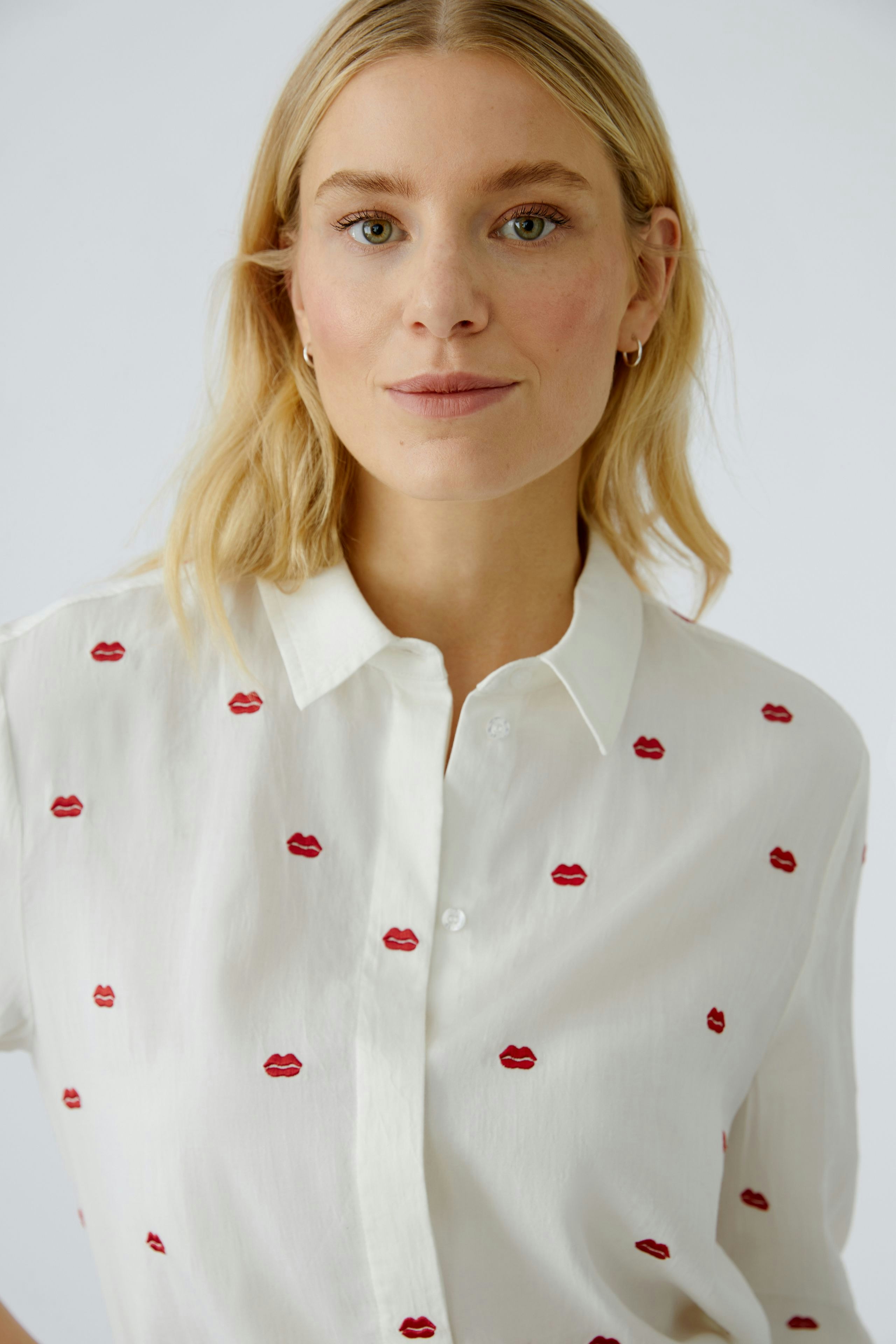 Casual women's blouse: A woman in a white shirt with red lip prints, smiling confidently.