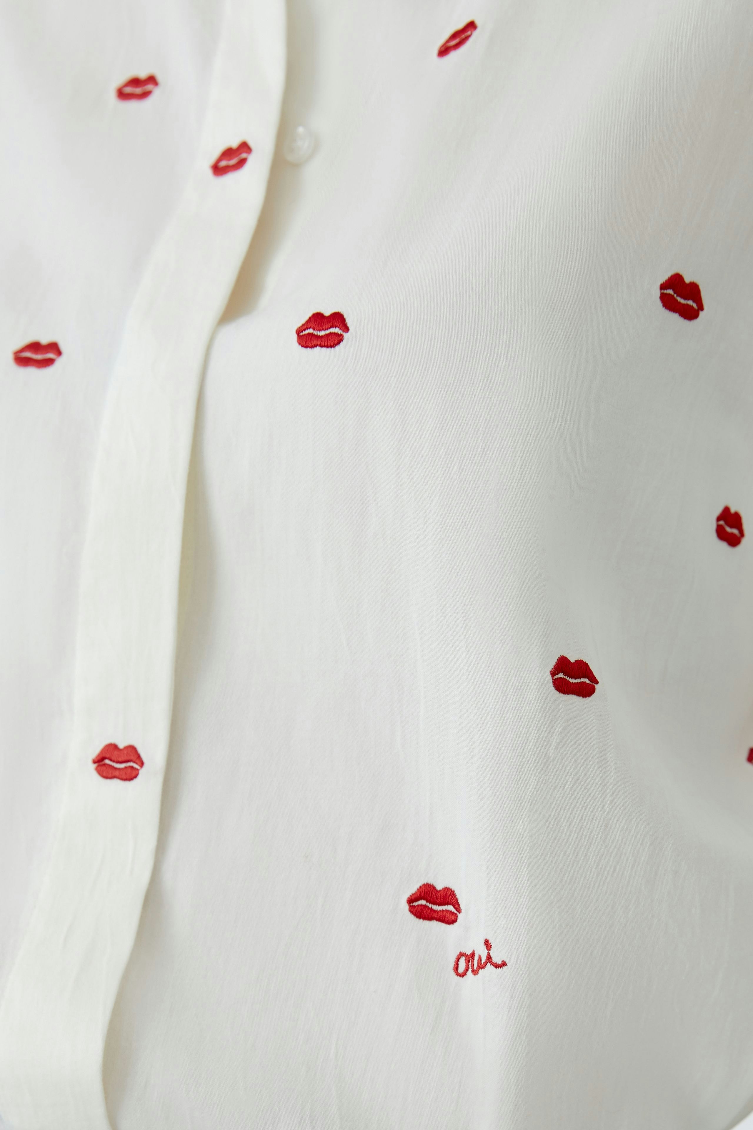 Casual women's blouse: Close-up of a white shirt with red lip embroidery, showcasing a playful design.
