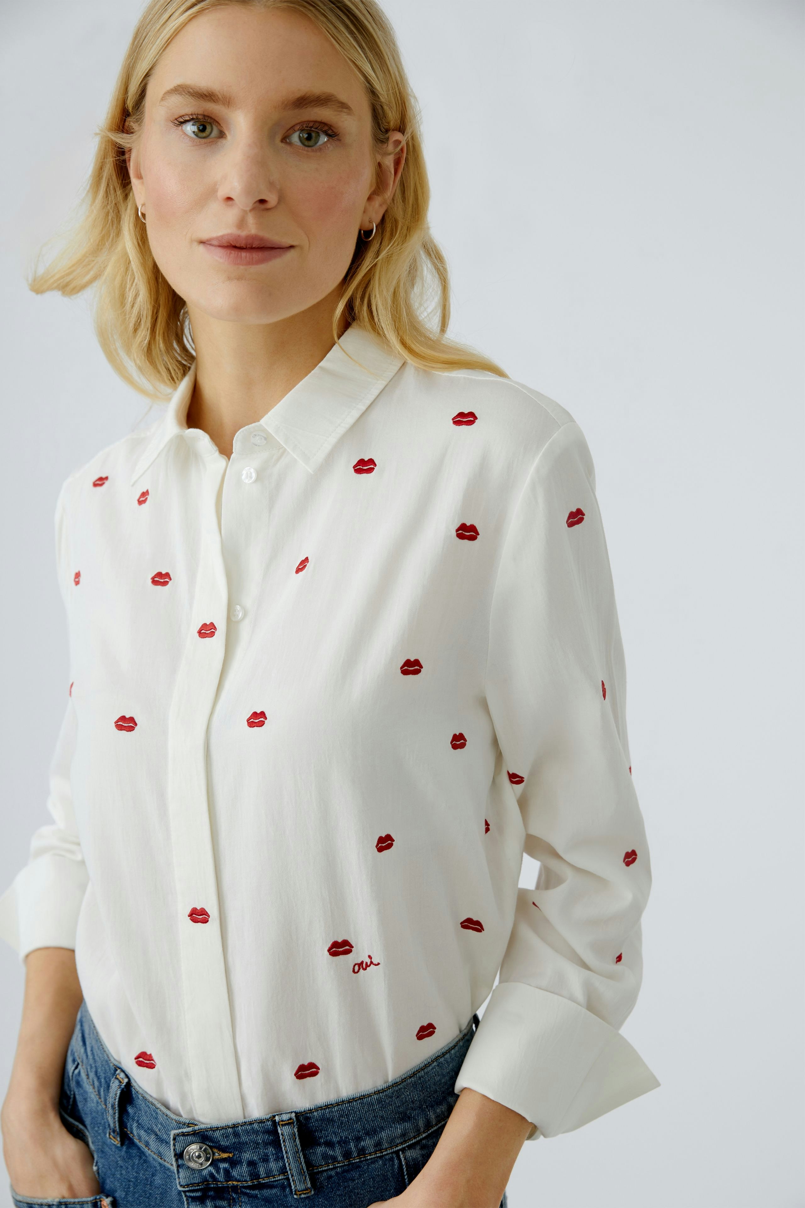 Casual women's blouse: A woman in a white shirt with red lips embroidery, paired with denim.