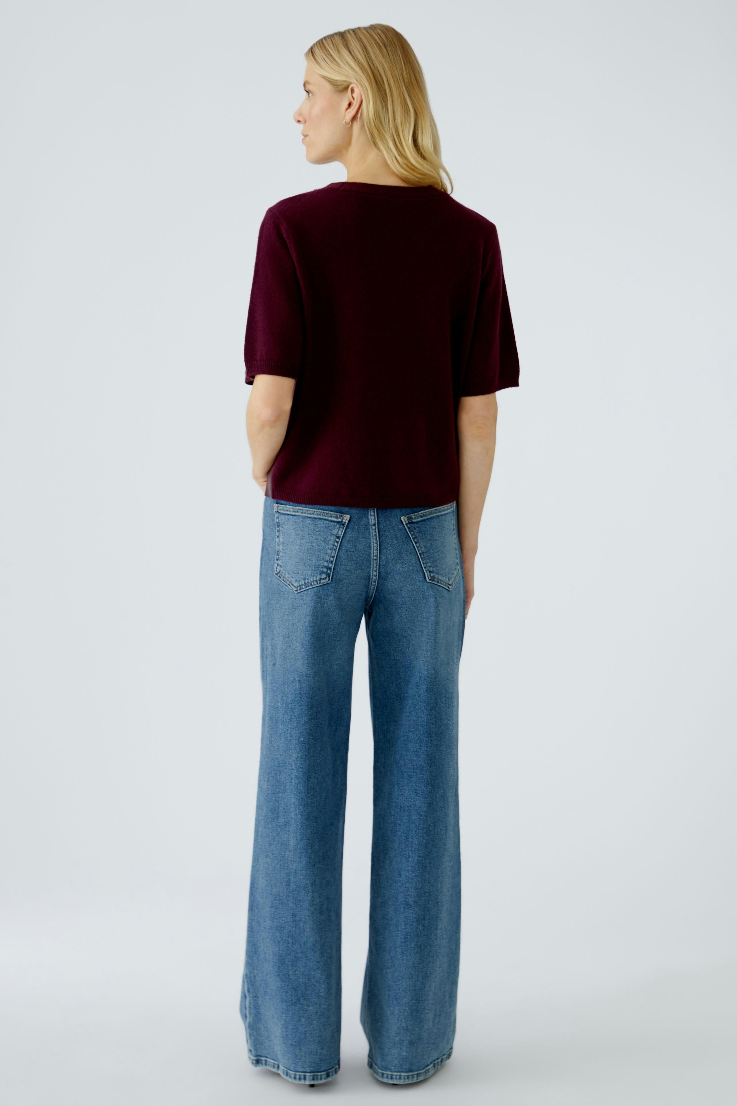Damen-Pullover in Bordeaux: Frau mit kurzen Ärmeln und lässiger Passform, kombiniert mit weiten Jeans.