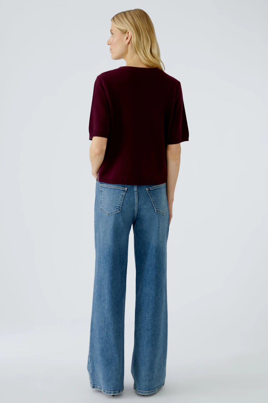 Damen-Pullover in Bordeaux: Frau mit kurzen Ärmeln und lässiger Passform, kombiniert mit weiten Jeans.