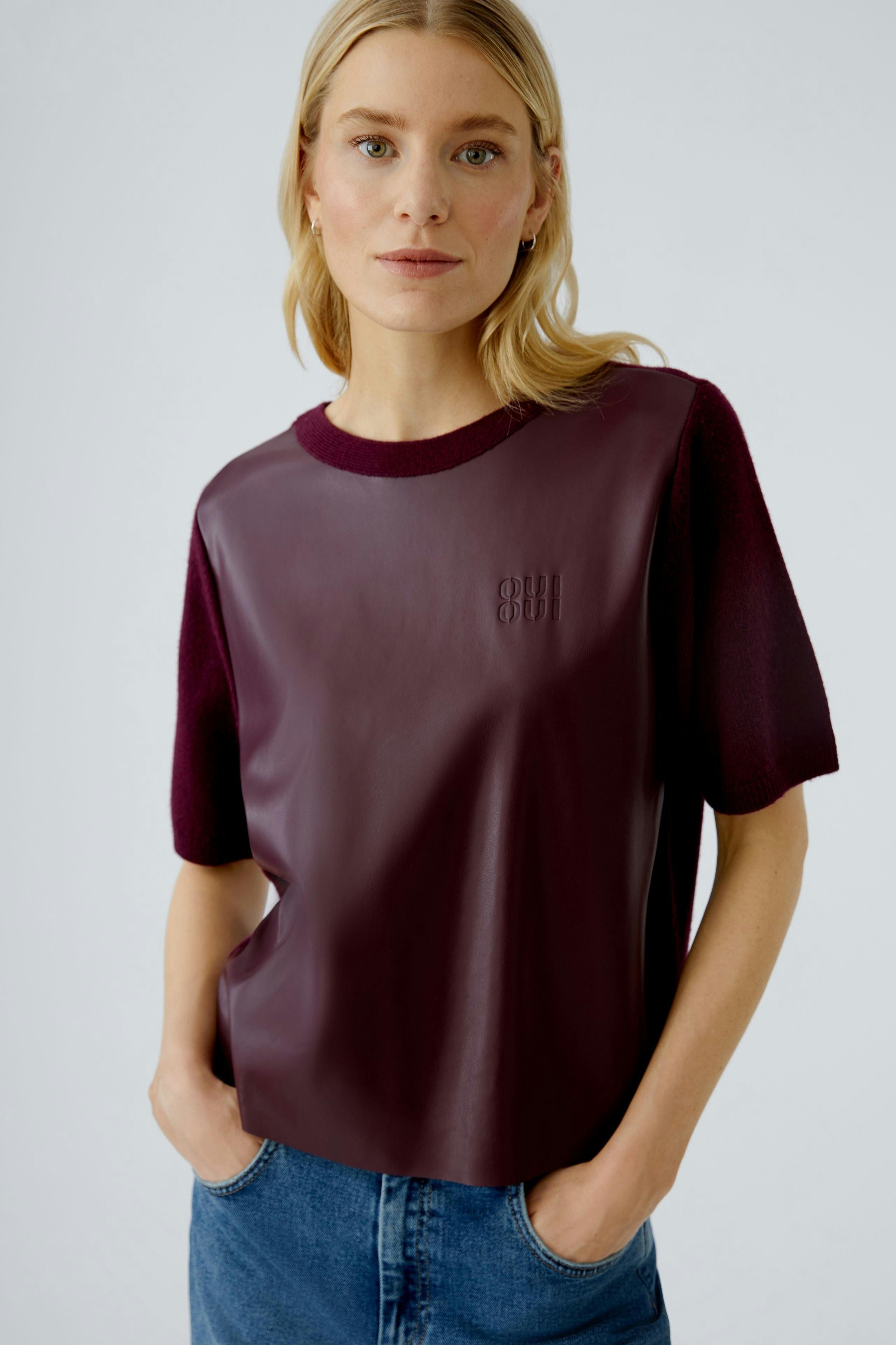 Damen-Pullover: Frau trägt einen burgunderfarbenen Pullover mit Lederoptik und lässigen Jeans.