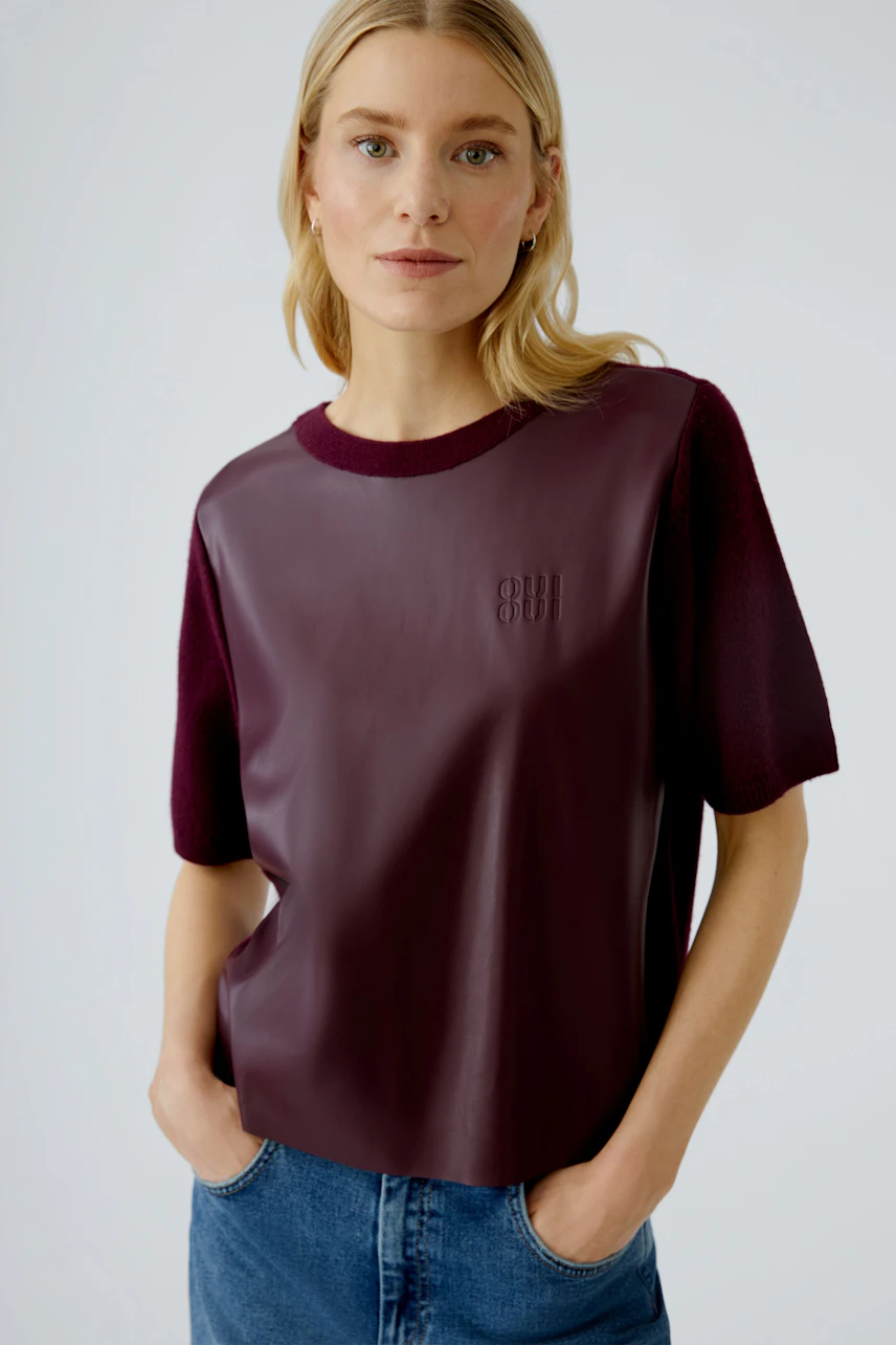 Damen-Pullover: Frau trägt einen burgunderfarbenen Pullover mit Lederoptik und lässigen Jeans.