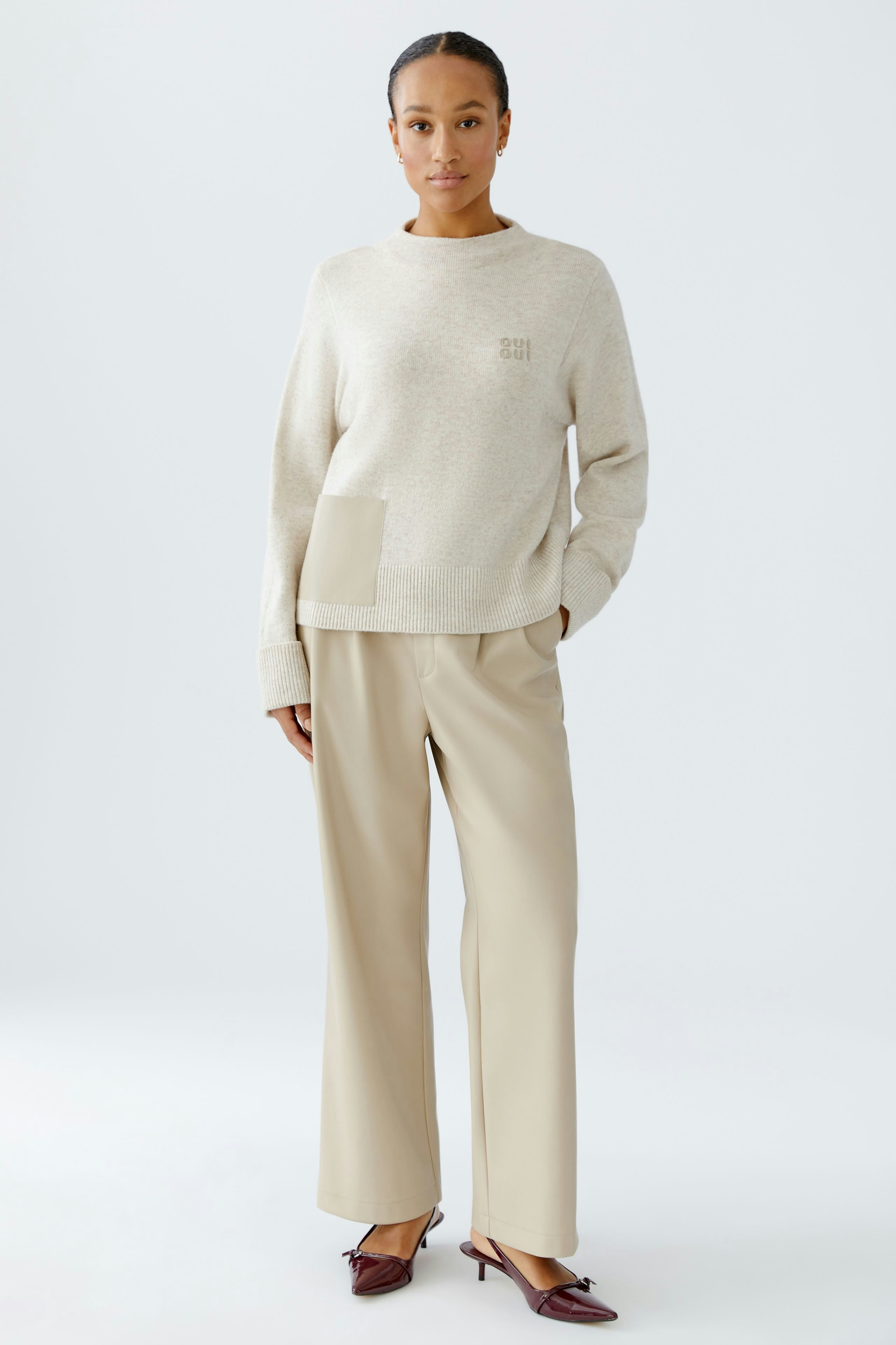 Casual women's pullover: A woman in a light beige pullover with a pocket, paired with wide trousers.