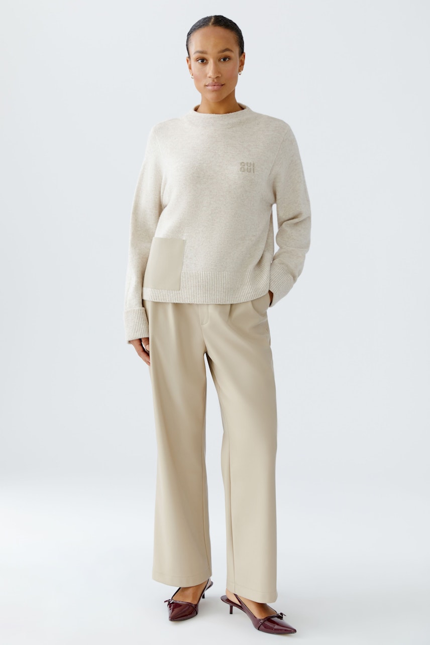 Bequemer Damen-Pullover in hellem Beige, kombiniert mit weiten, hellen Hosen. Die Frau trägt einen lässigen Look.