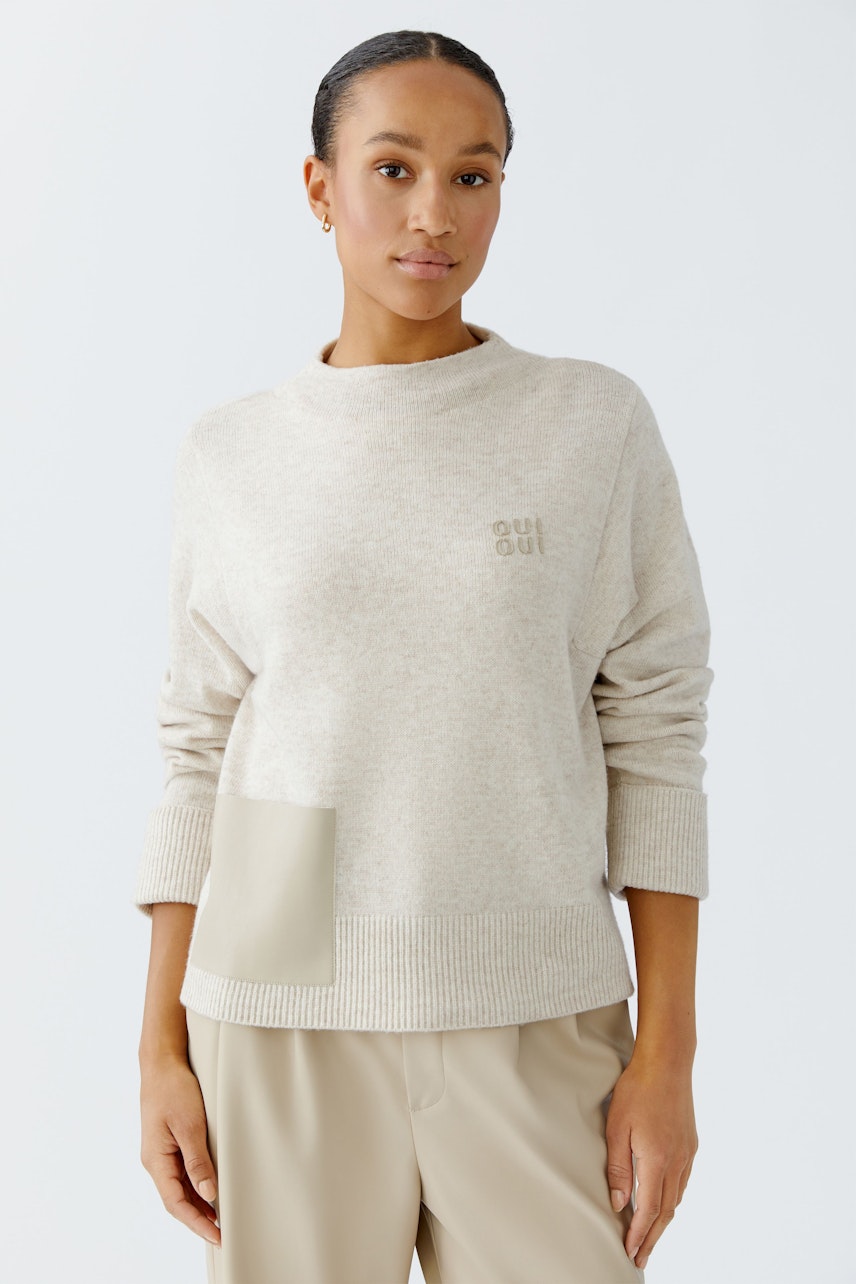 Beiger Damen-Pullover: Frau trägt einen lässigen Pullover mit einer praktischen Tasche und einem modernen Schnitt.