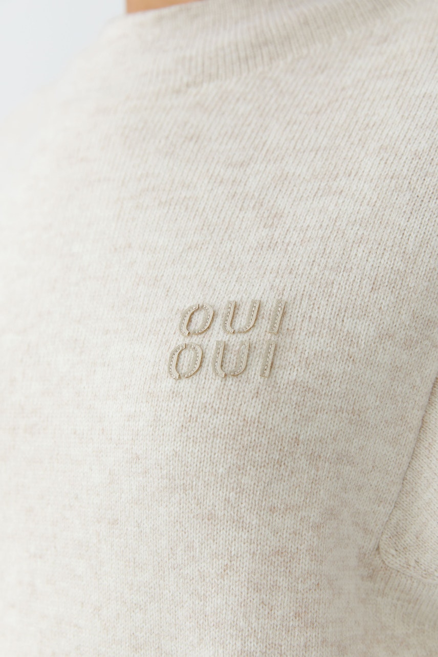 Beiger Damen-Pullover: Frau trägt einen bequemen, lässigen Pullover mit dezentem Logo.
