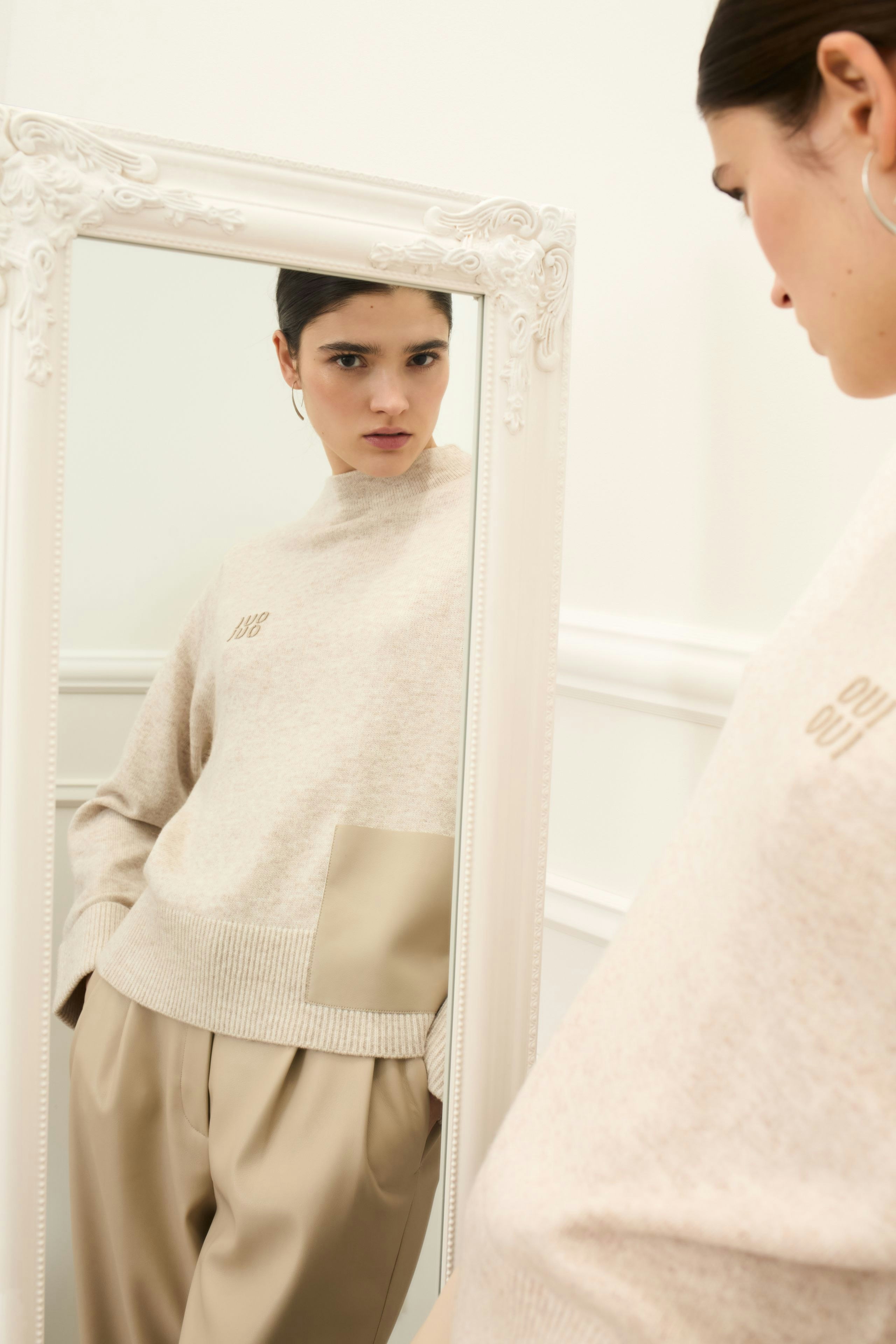 Casual women's pullover: Young woman in a beige pullover with a stylish pocket, looking in a mirror.