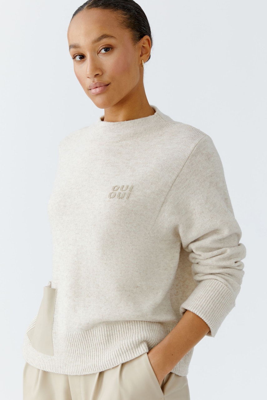Beiger Damen-Pullover: Frau trägt einen lässigen Strickpullover mit dezentem Logo und bequemen Schnitt.