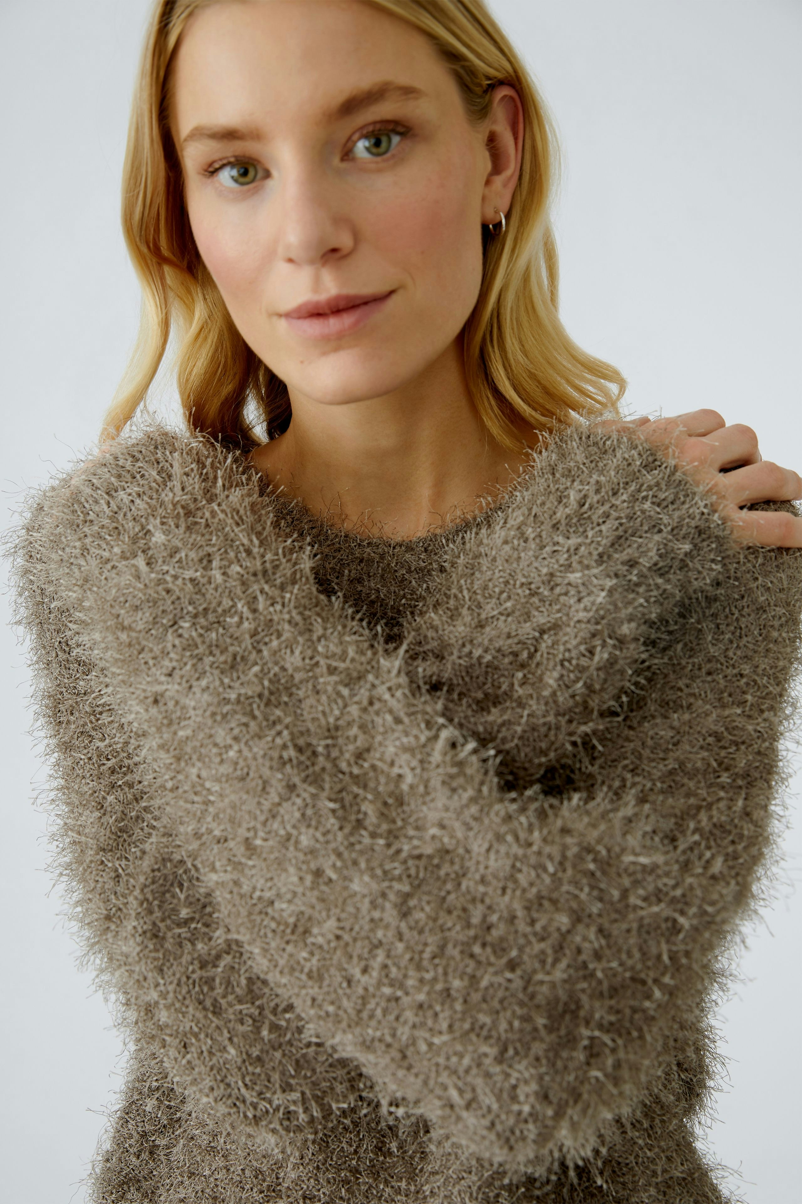 Cozy women's pullover: A woman in a soft, fuzzy brown pullover with relaxed sleeves.