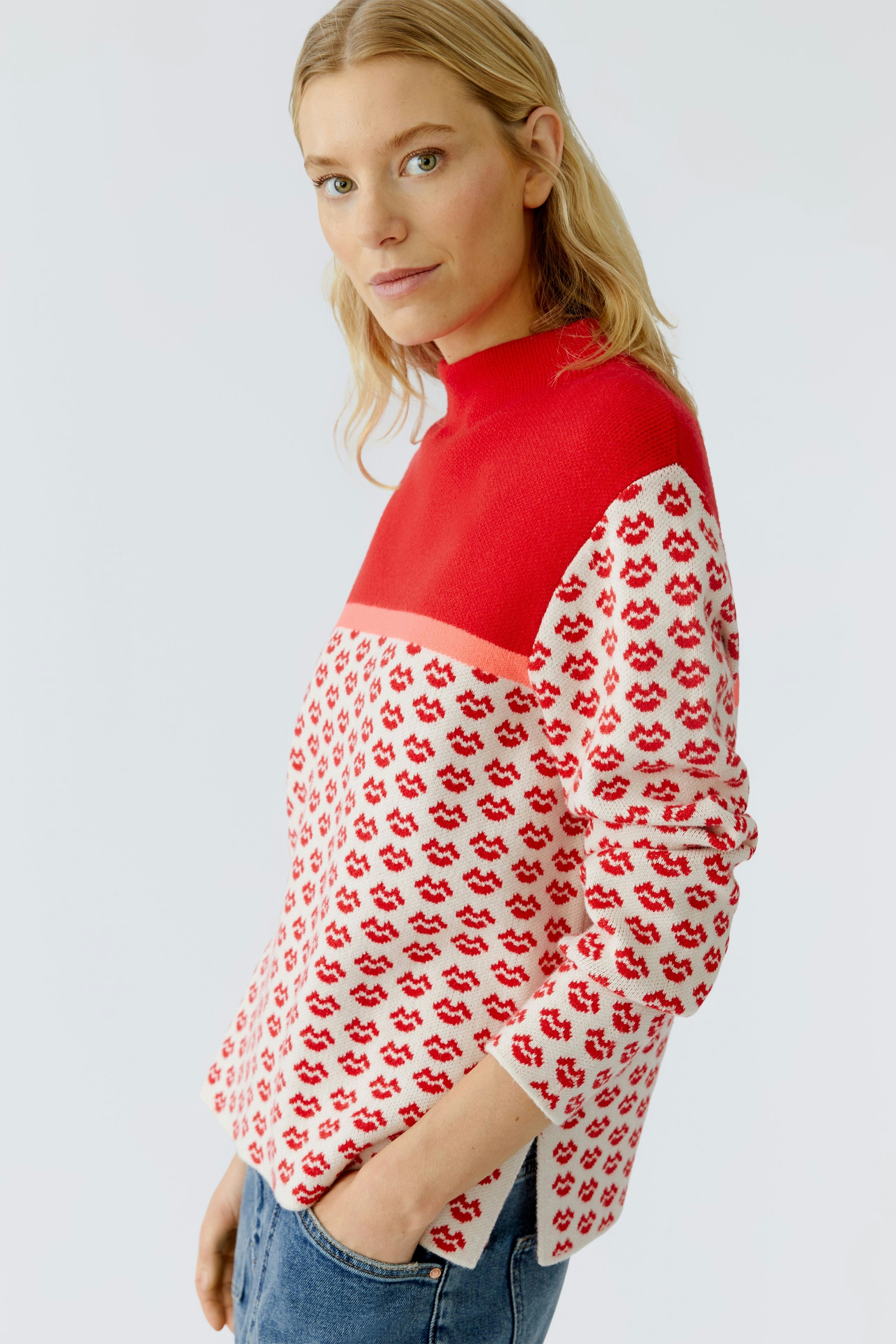 Modern pullover: Woman in a red and white patterned pullover with a high neck, smiling confidently.