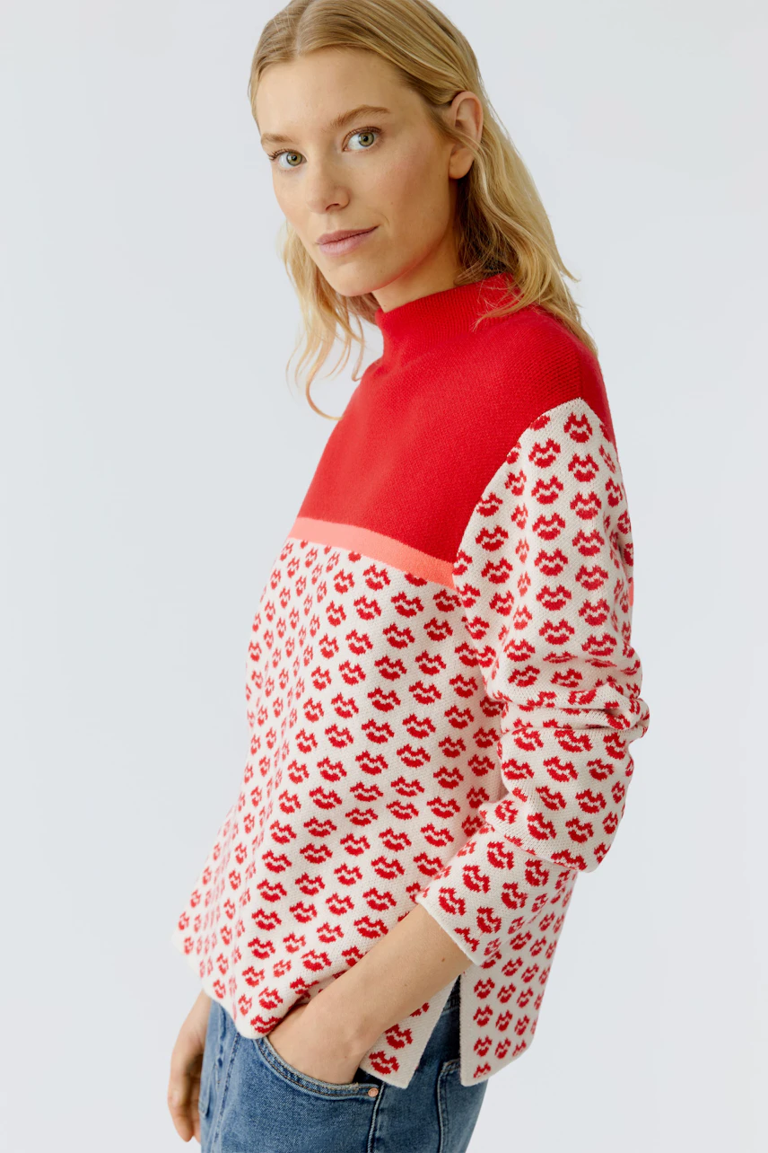 Modern pullover: Woman in a red and white patterned pullover with a high neck, smiling confidently.