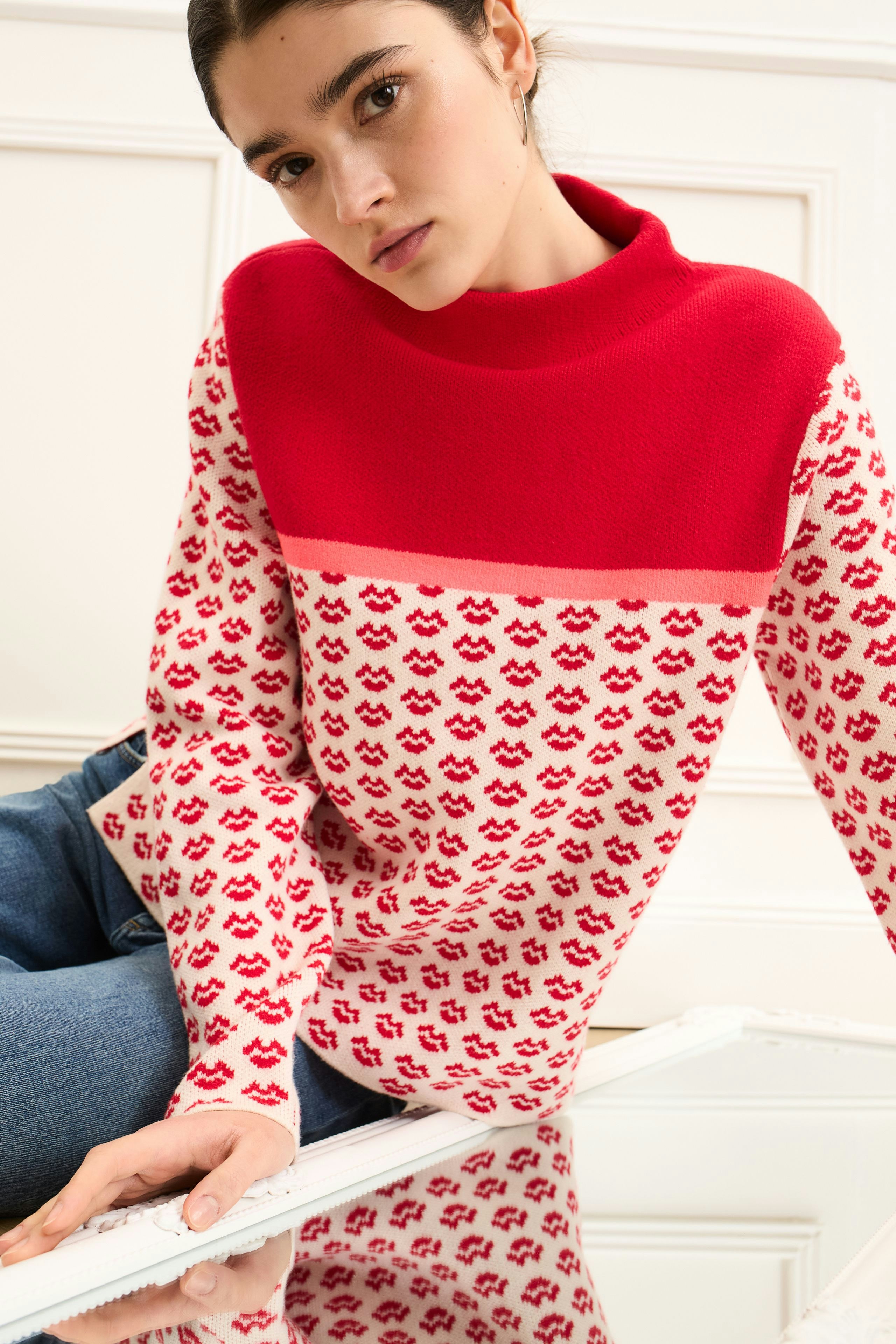 Modern women's pullover: Young woman in a red and white patterned pullover with a high collar.