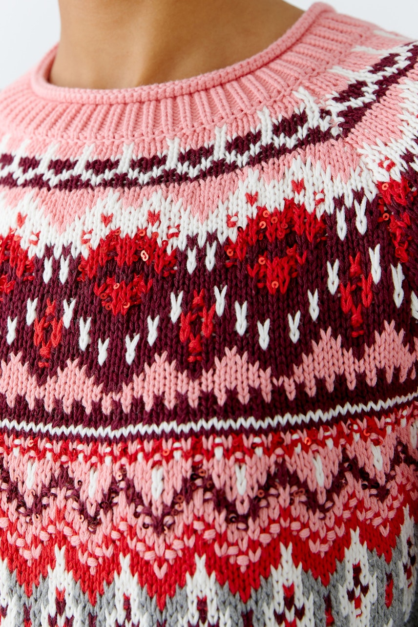 Bunter Damen-Pullover: Nahaufnahme eines pinken Strickpullovers mit geometrischem Muster.
