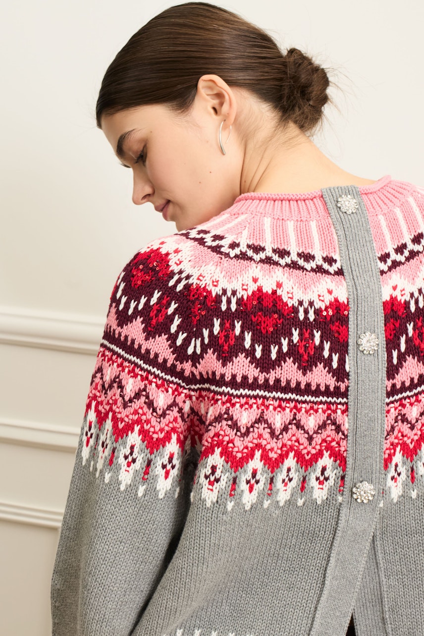Damen-Pullover: Frau mit buntem Strickpullover in Grau, Pink und Rot, mit dekorativen Knöpfen am Rücken.