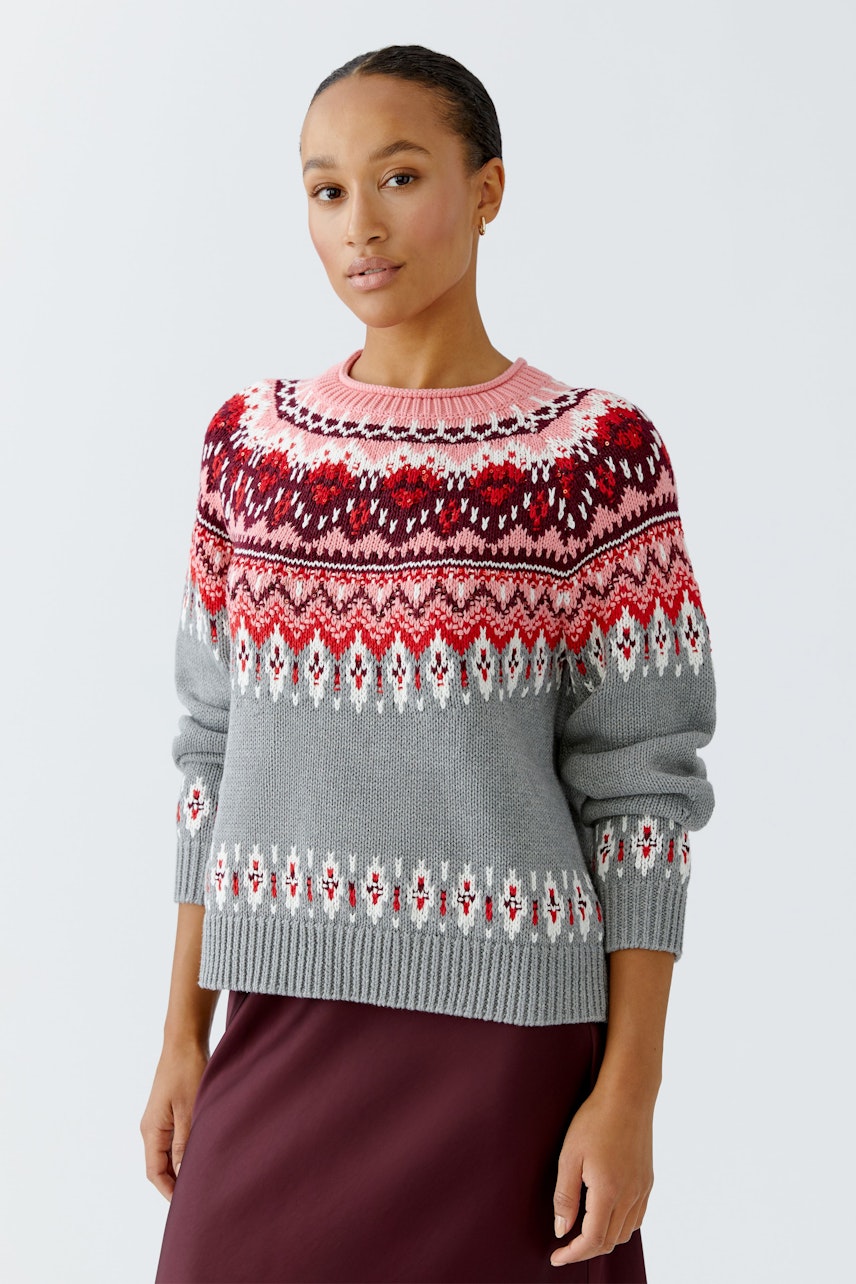 Damen-Pullover: Frau trägt grauen Pullover mit buntem Muster und lässigem Schnitt.