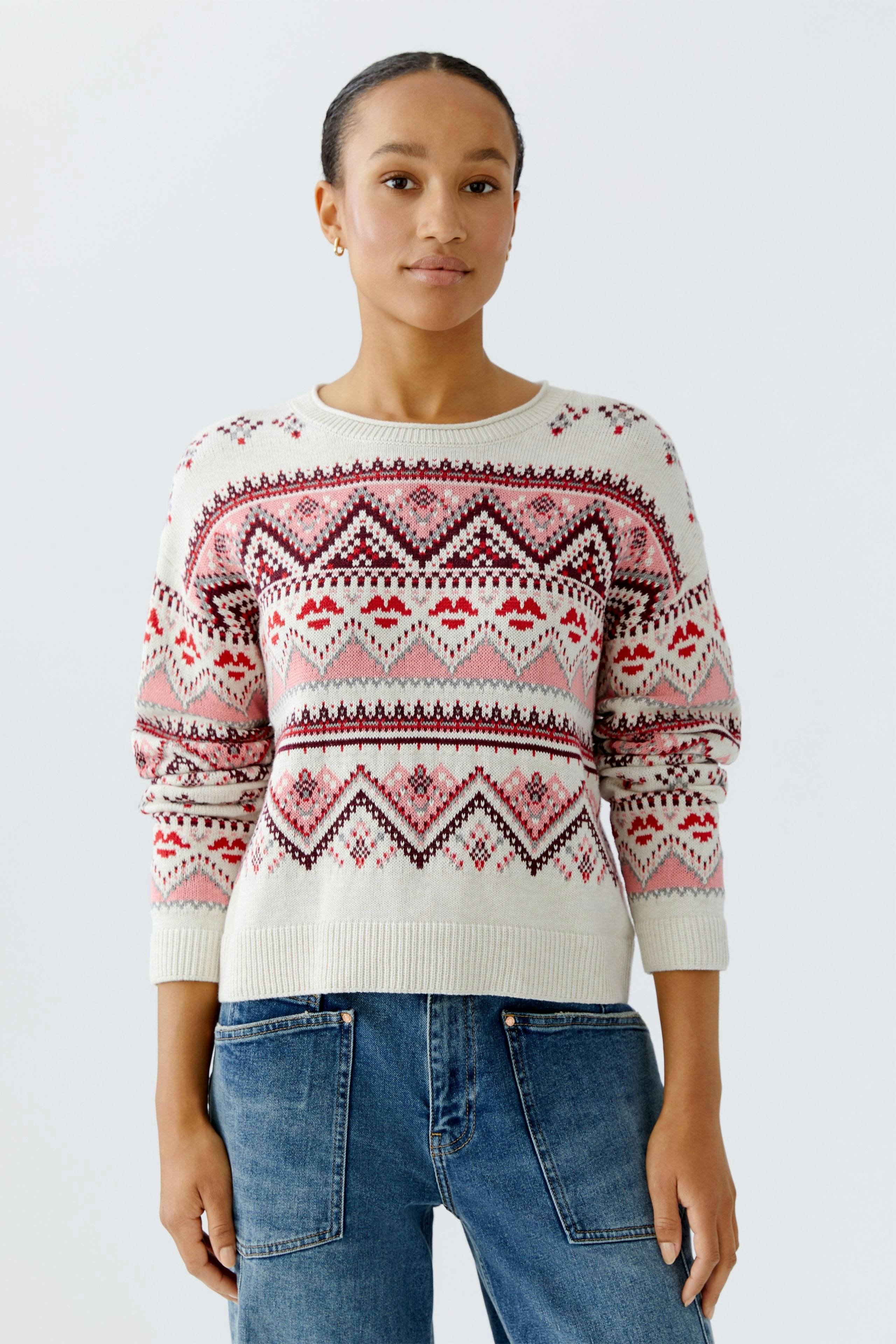 Casual women's pullover: Young woman in a patterned pullover with red and pink designs, paired with jeans.