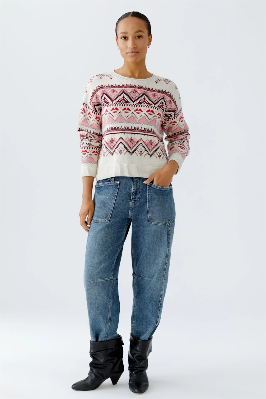Damen-Pullover: Frau in buntem Strickpullover mit geometrischem Muster und lässigen Jeans.