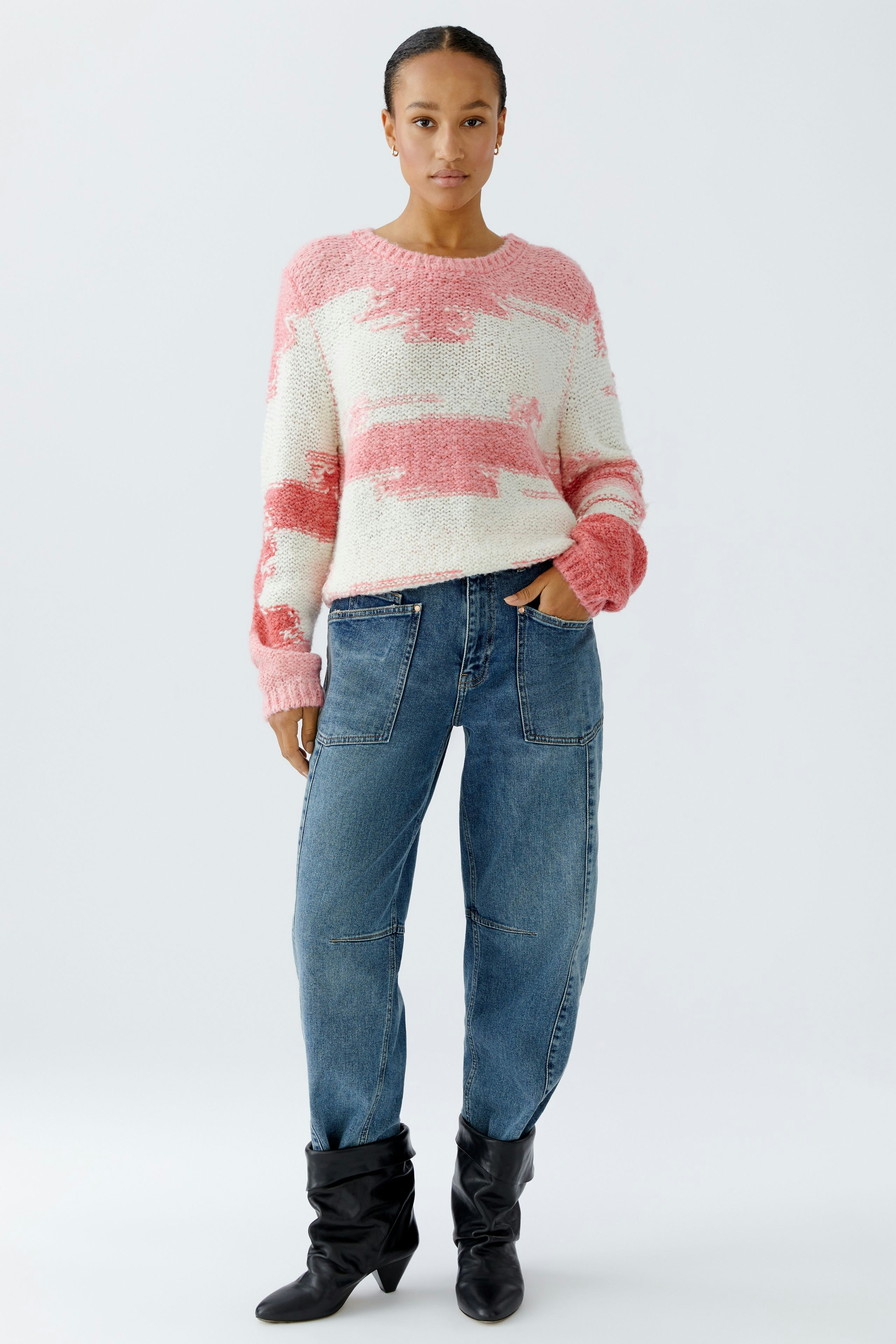 Damen-Pullover: Frau in rosa-weißem Strickpullover mit lässigen Jeans und Stiefeln.