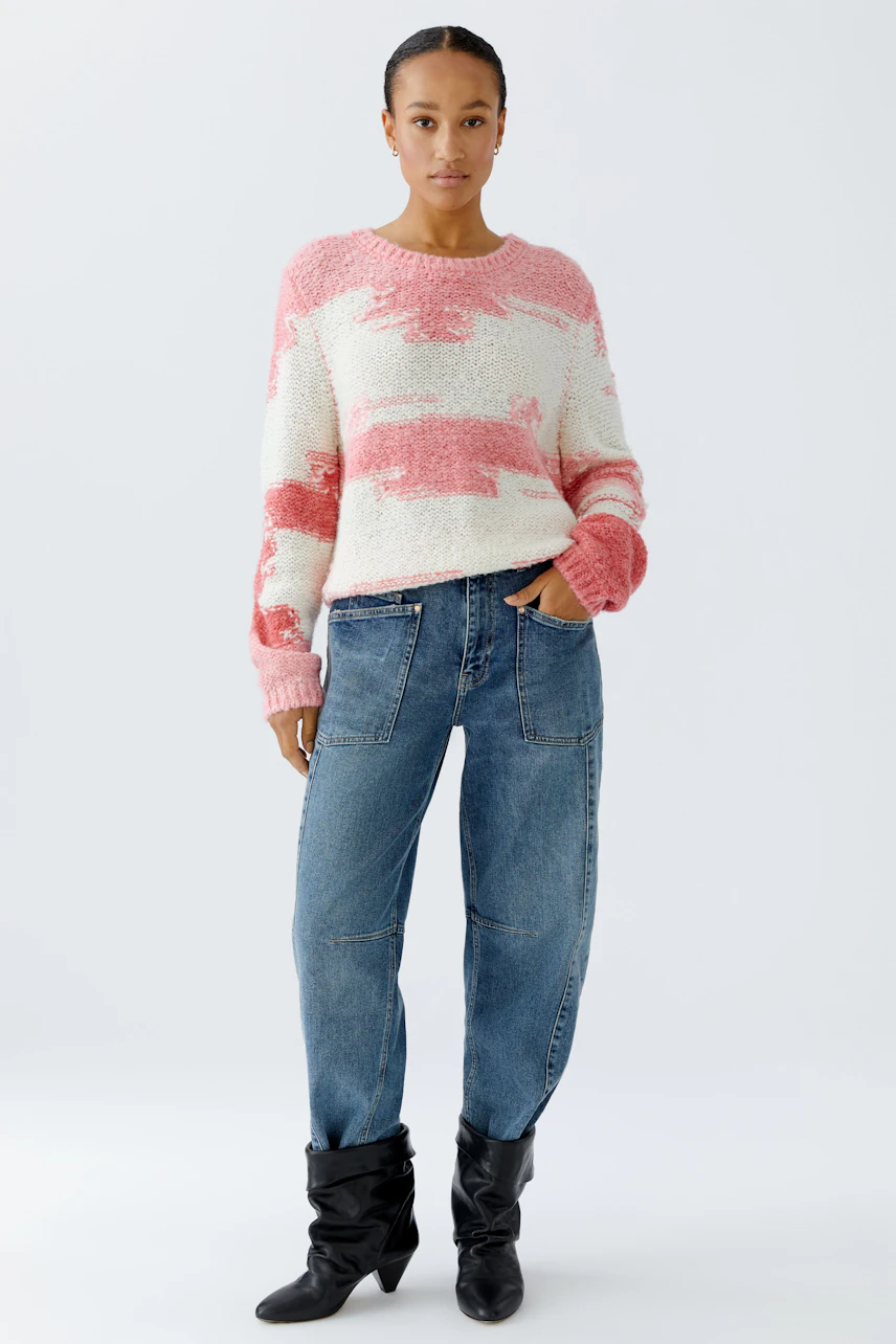 Damen-Pullover: Frau in rosa-weißem Strickpullover mit lässigen Jeans und Stiefeln.