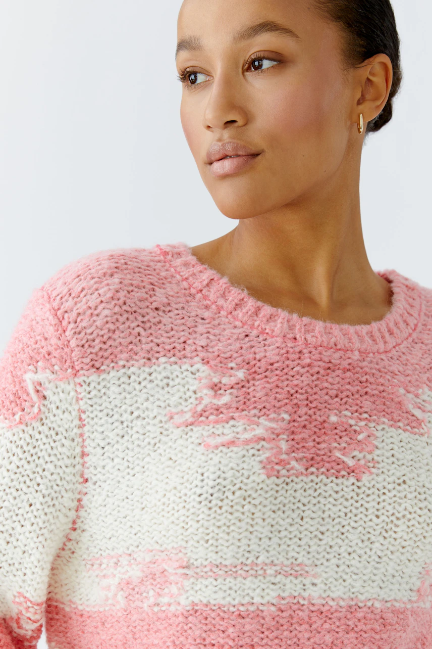 Damen-Pullover: Frau trägt einen lässigen, rosa-weißen Strickpullover mit modernem Muster.