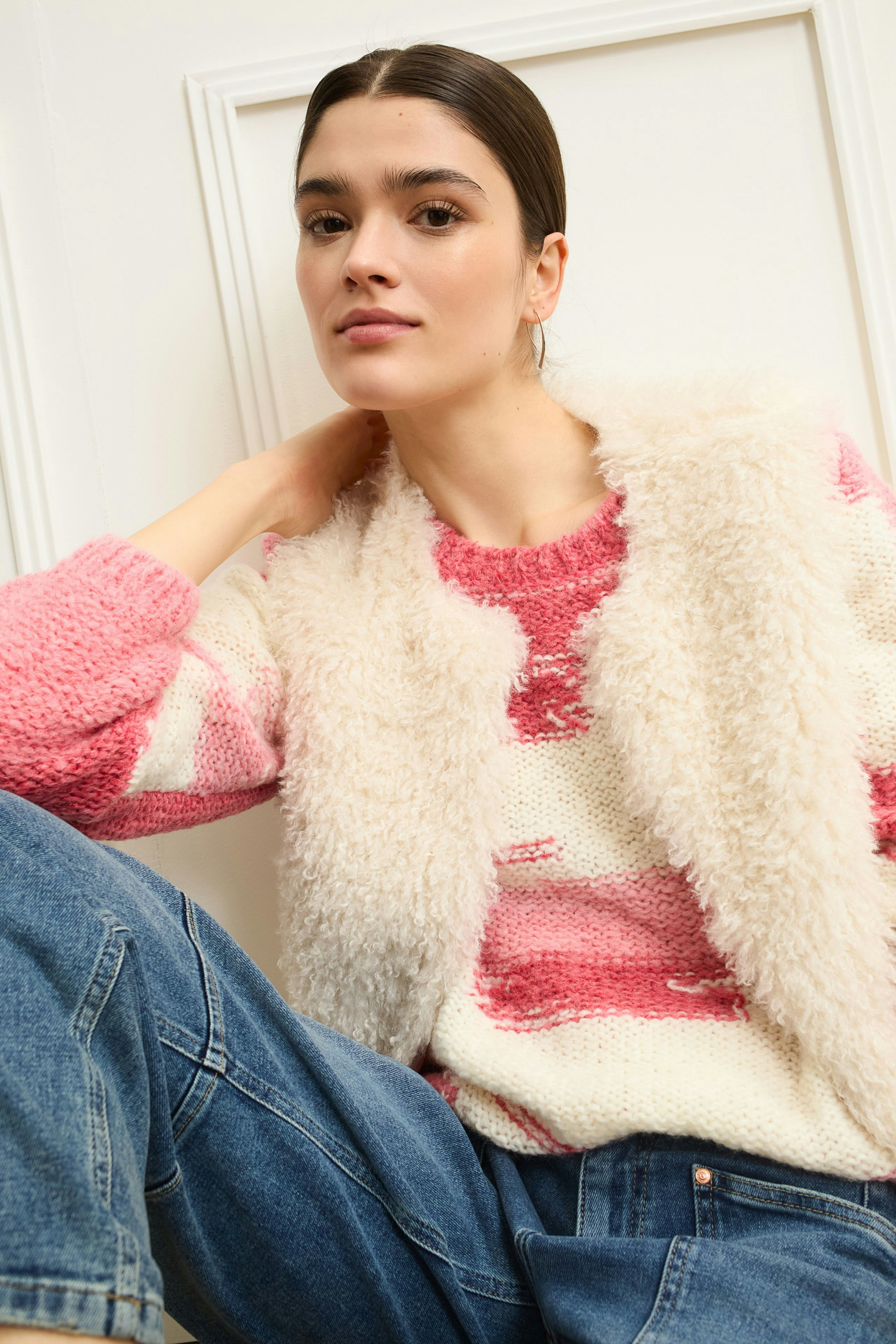 Damen-Pullover: Frau in pink-weiß gestreiftem Strickpullover mit lässiger Weste und Jeans.