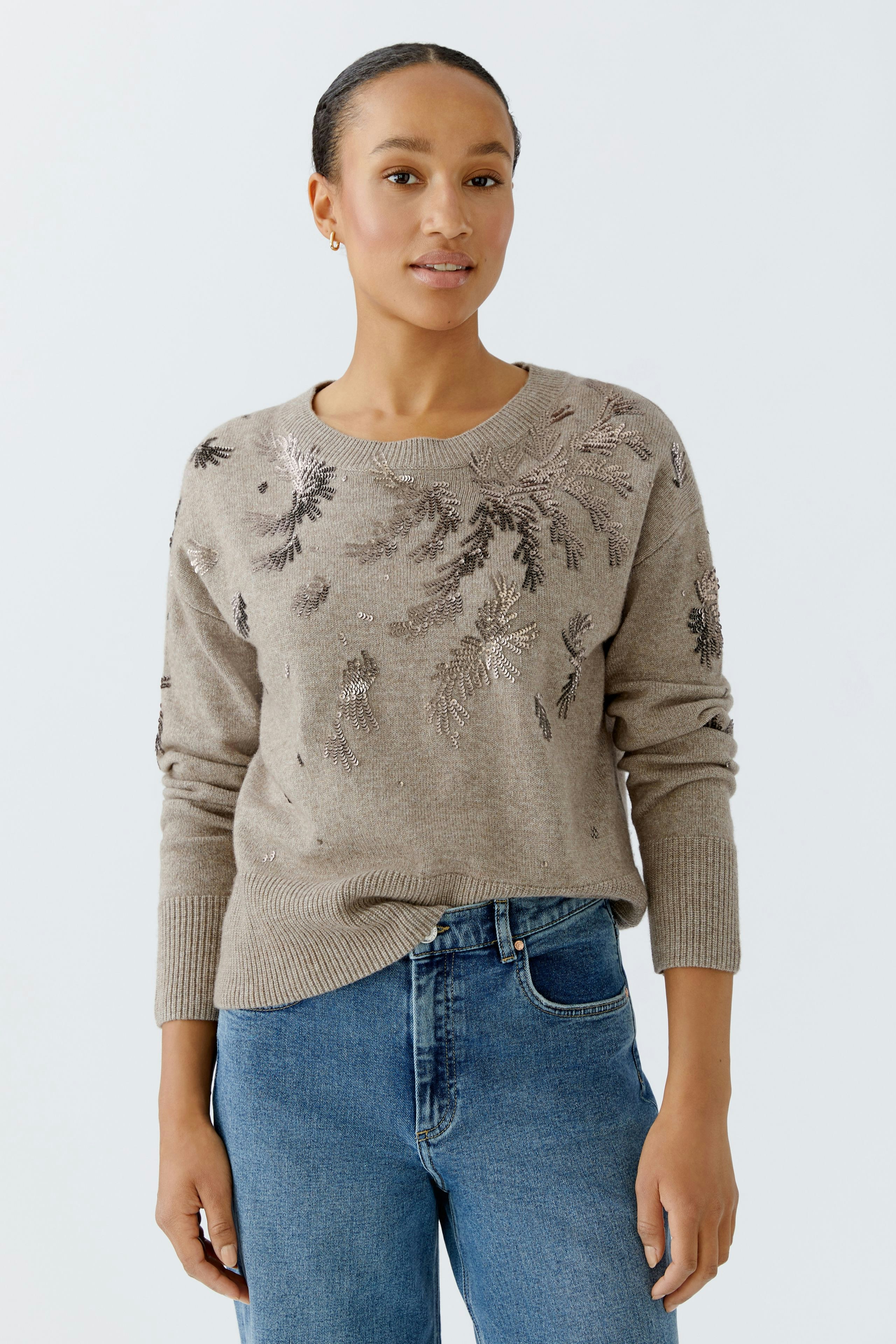 Damen-Pullover: Junge Frau in beigem Strickpullover mit floralem Muster und lässigen Jeans.