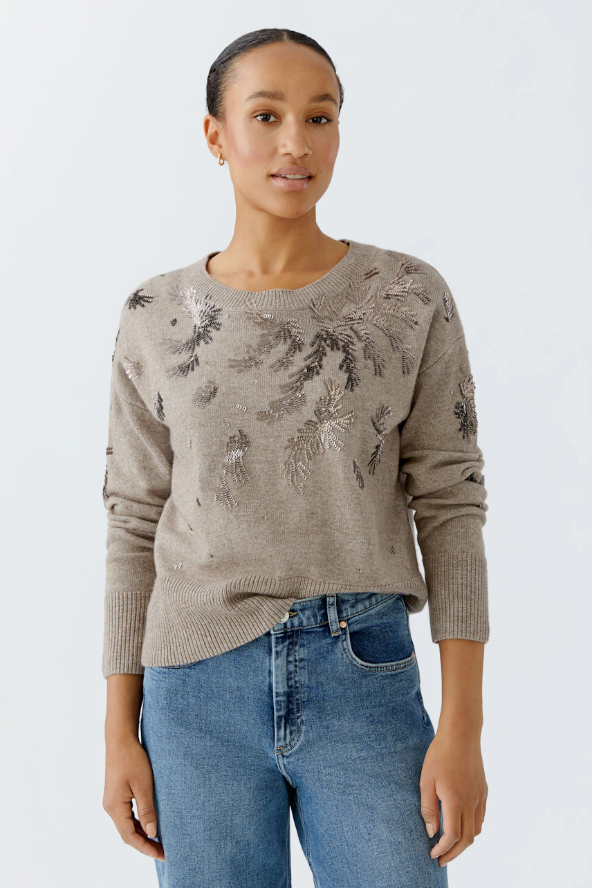 Damen-Pullover: Junge Frau in beigem Strickpullover mit floralem Muster und lässigen Jeans.