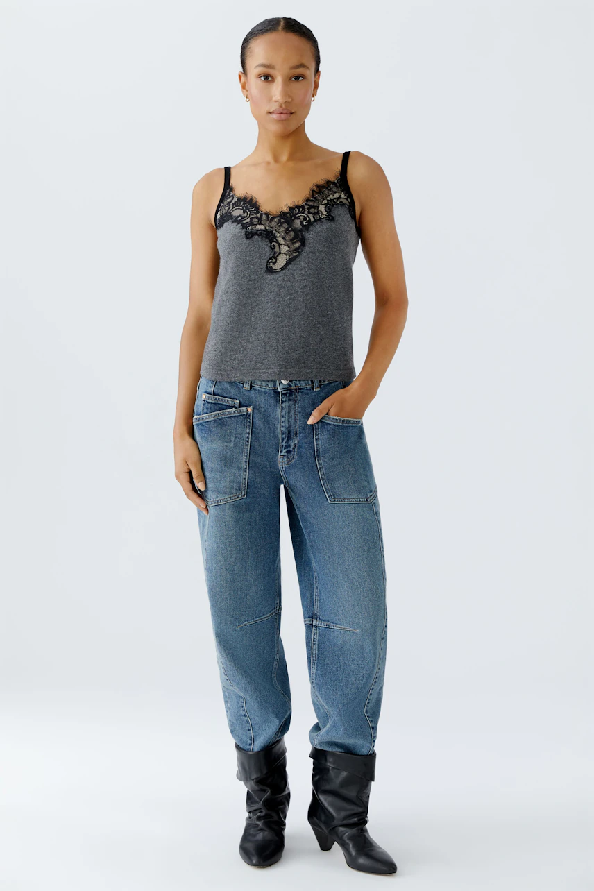 Damen-Top: Frau in grauem Top mit Spitzenbesatz und lässigen Jeans steht selbstbewusst.