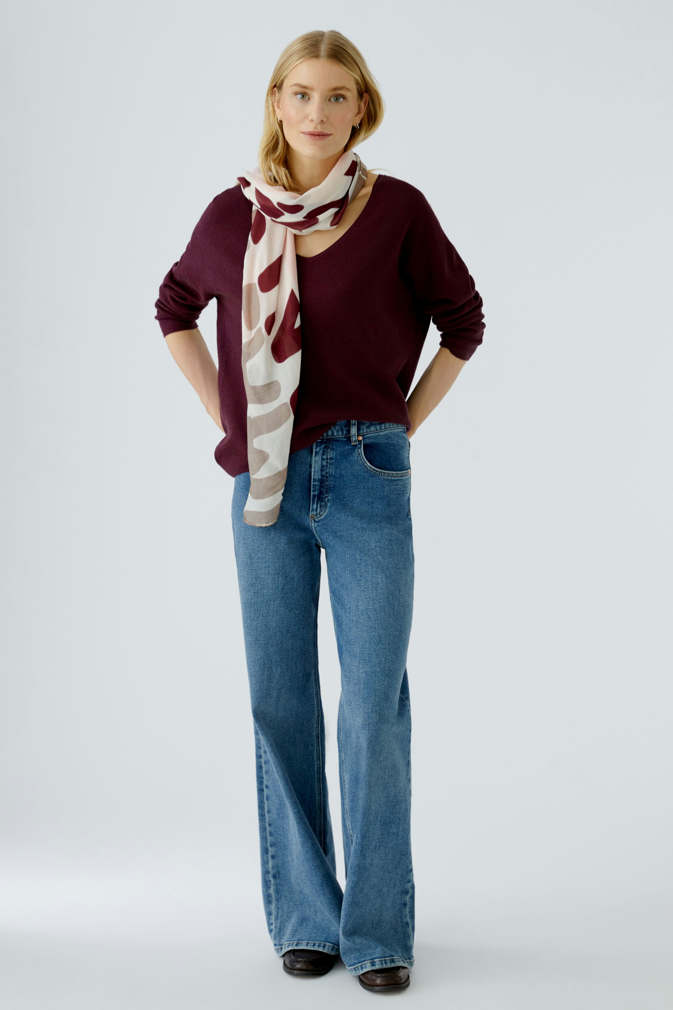 Casual women's pullover: Woman in a burgundy pullover with a light scarf and flared jeans.