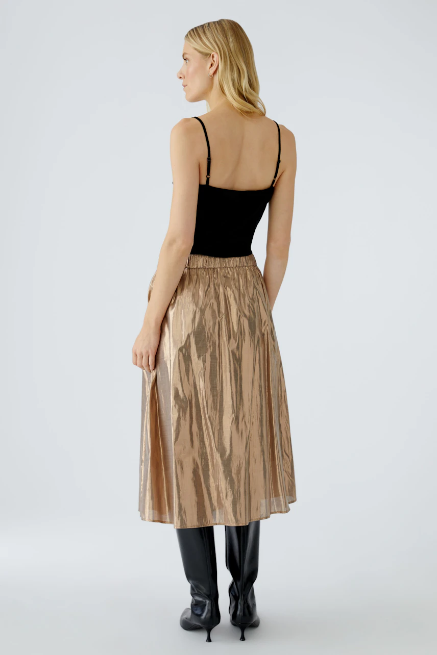 Shiny pleated skirt: Woman wearing a metallic gold pleated skirt with a black top and stylish boots.