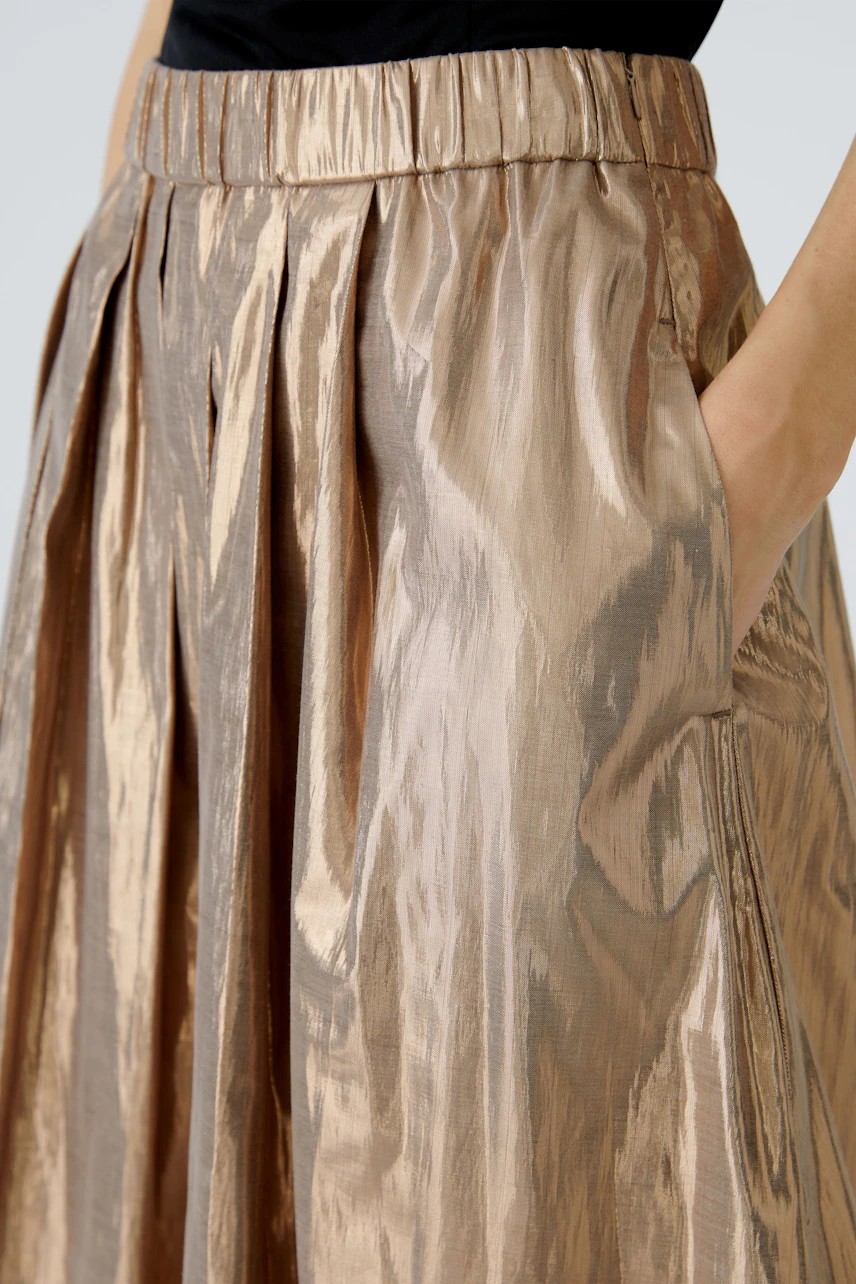 Shiny pleated skirt: A woman showcases a metallic bronze skirt with a comfortable waistband and pockets.
