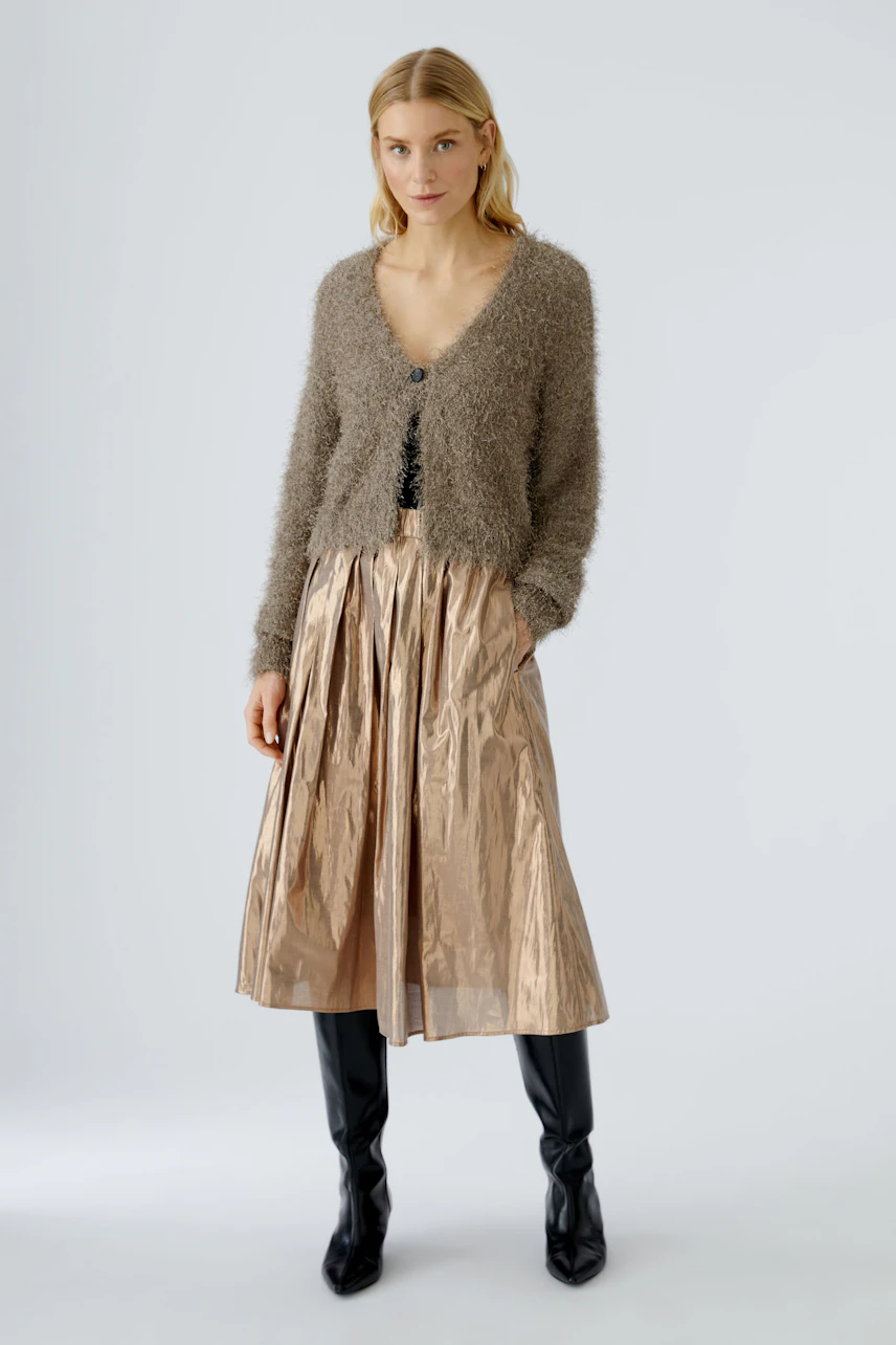 Modern pleated skirt: Woman in a shiny, light brown pleated skirt paired with a cozy cardigan.