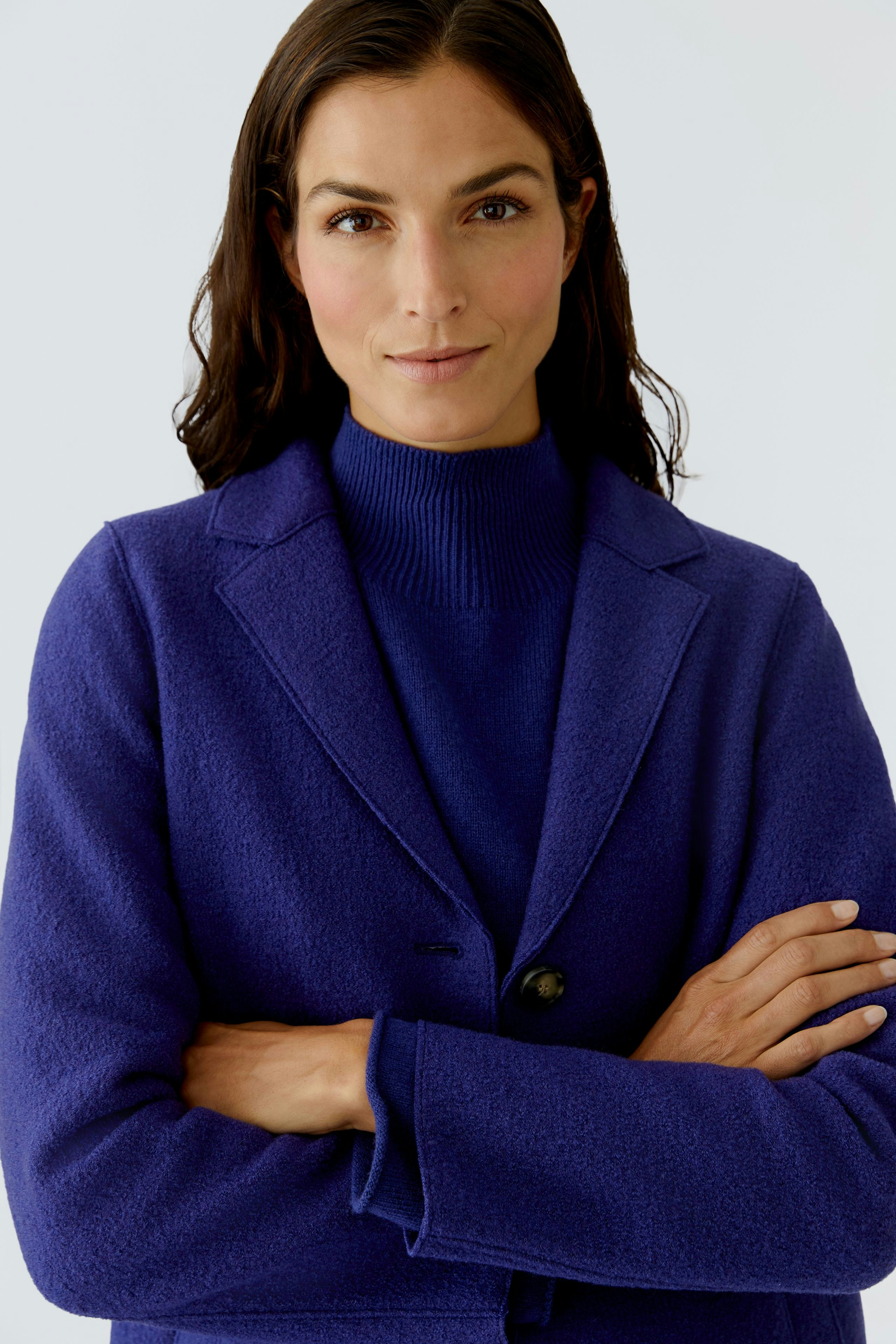 Wool coat: Woman in a purple wool coat over a striped pullover, smiling with arms crossed.