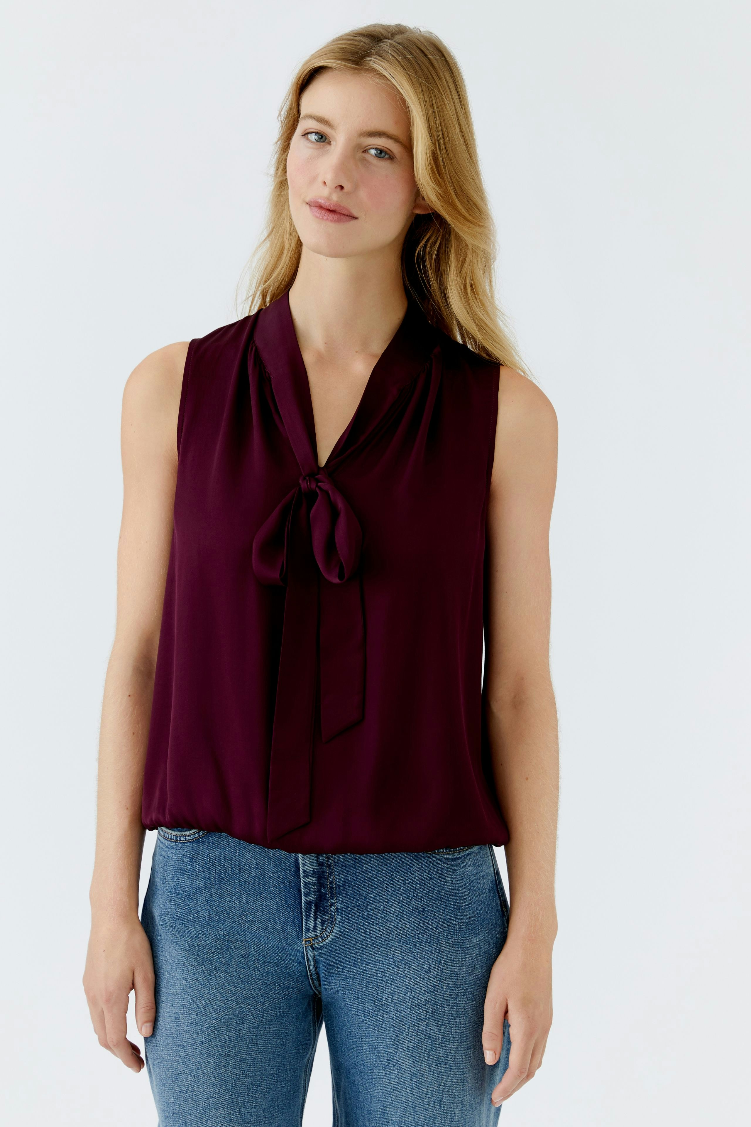 Sleeveless blouse: Woman in a burgundy blouse with a tie detail, paired with casual jeans.