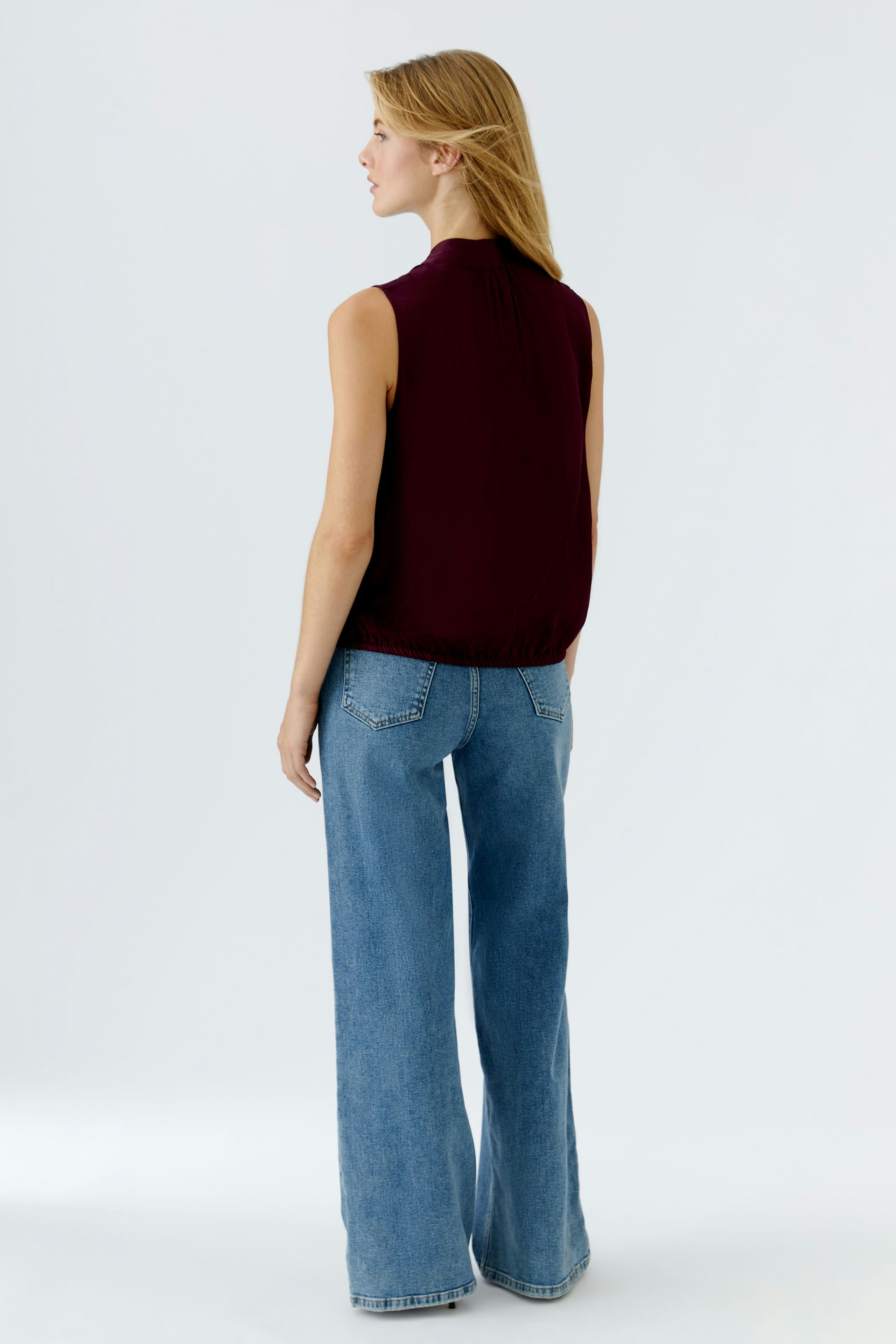 Casual women's blouse: Woman in a burgundy blouse paired with wide-leg jeans, showcasing a relaxed style.