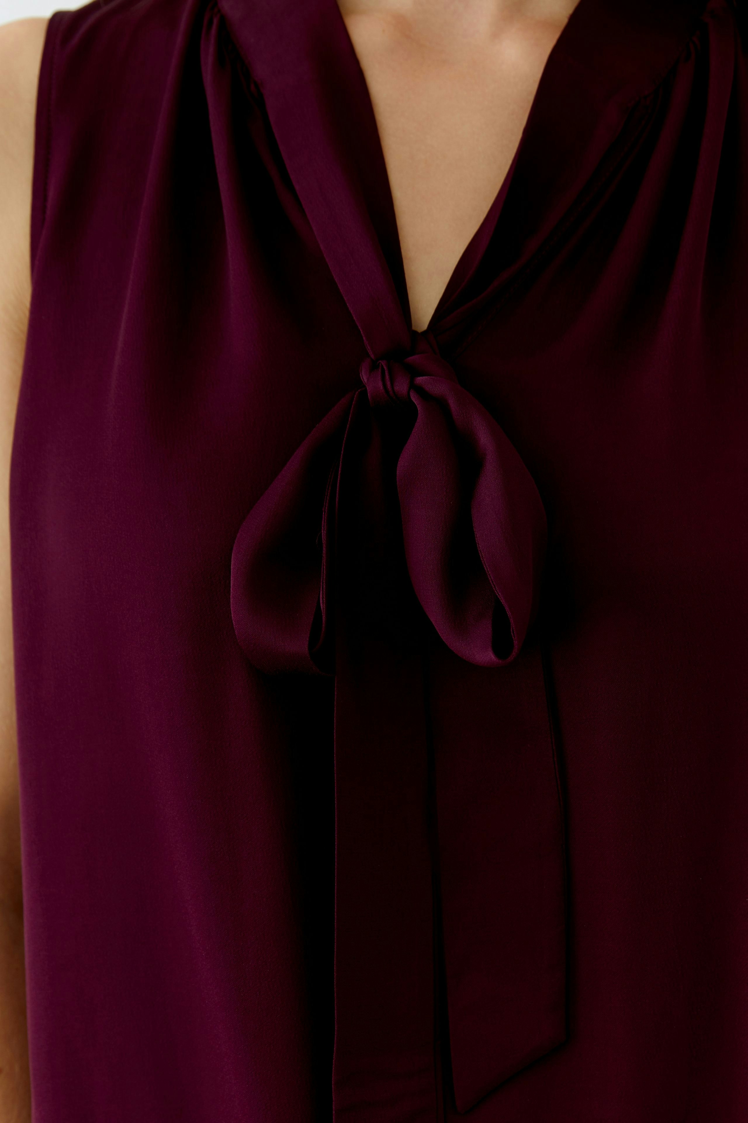 Stylish women's blouse: Close-up of a woman in a burgundy blouse with a bow tie detail.