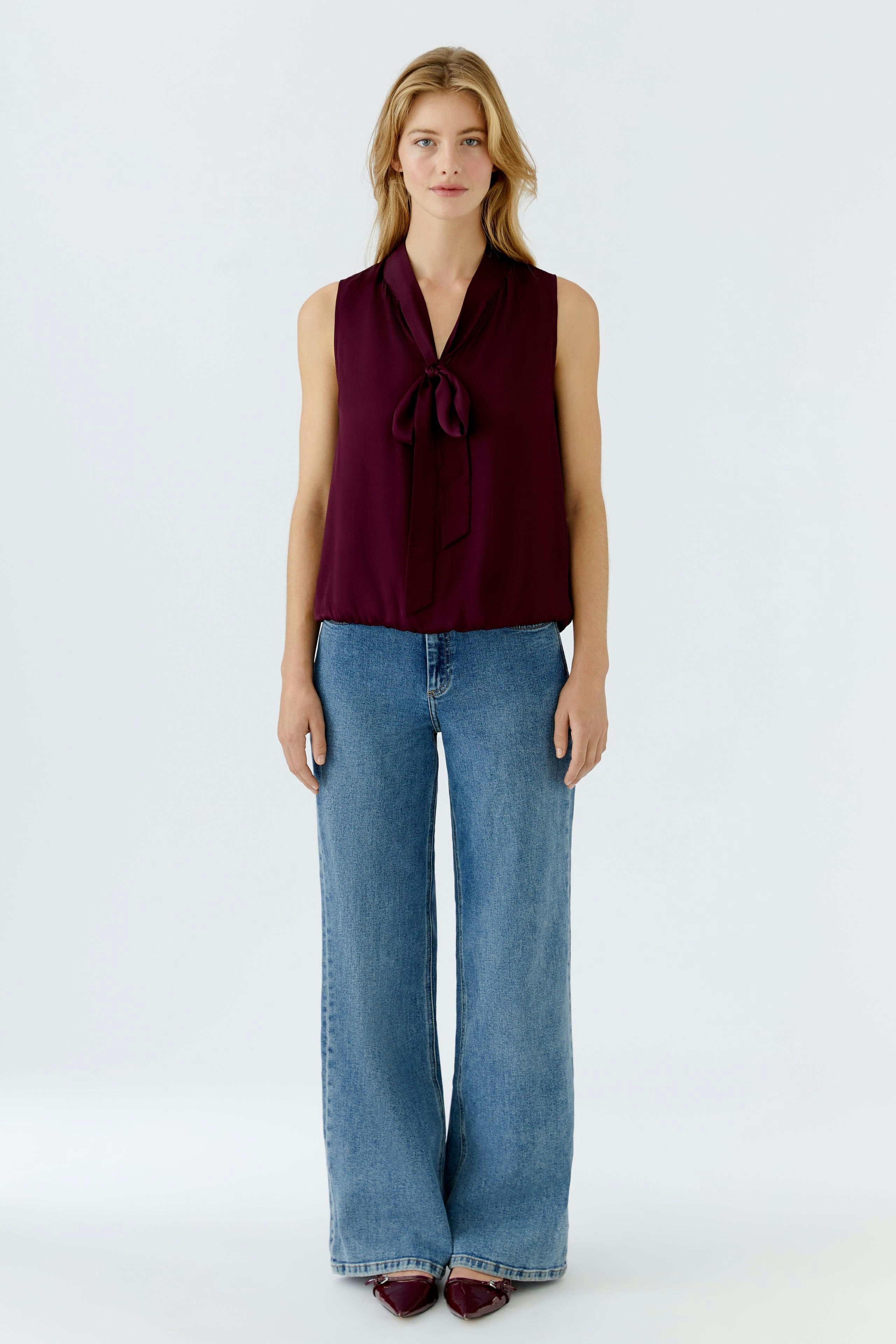 Chic women's blouse: A woman in a burgundy tie-neck blouse paired with wide-leg jeans.
