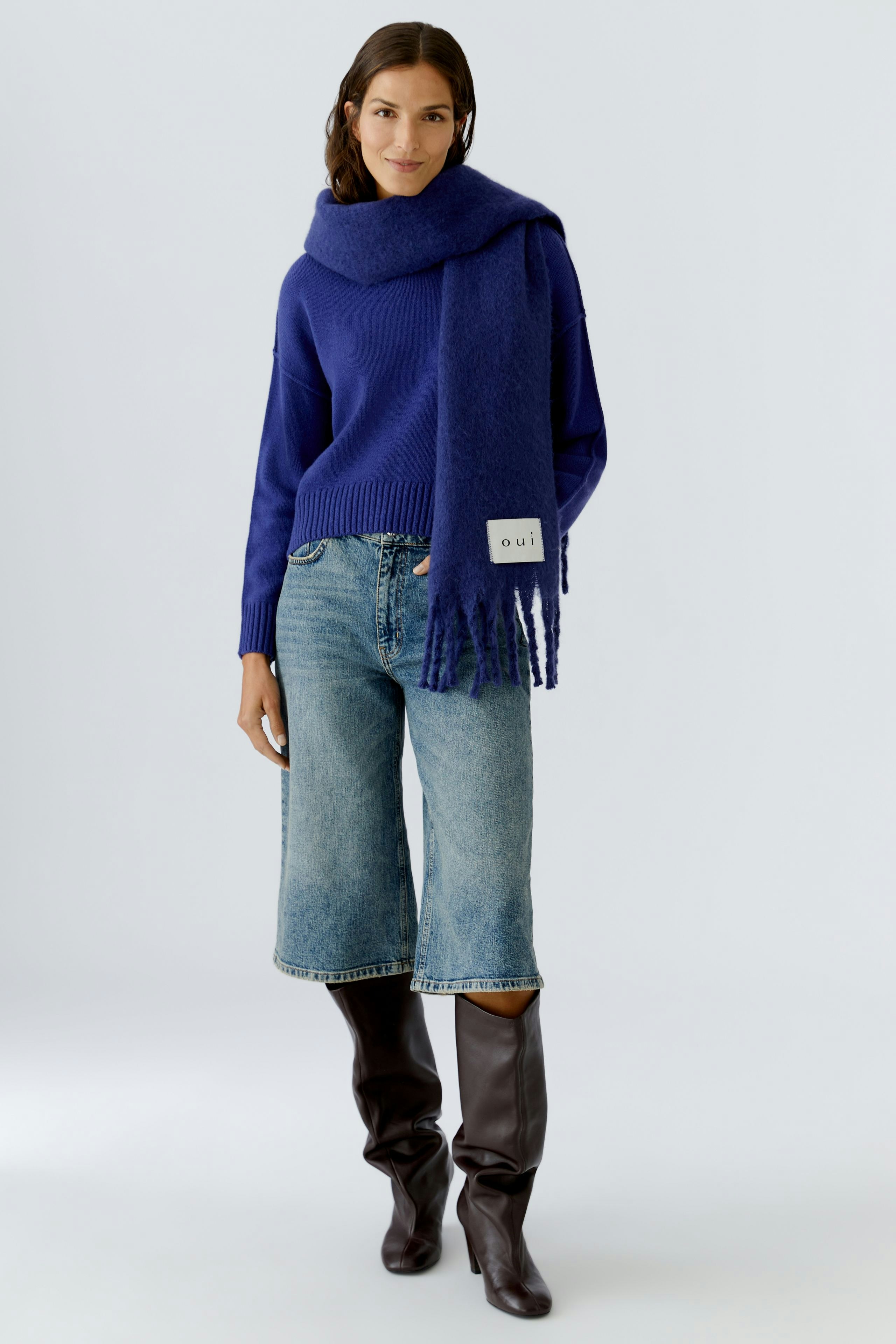 Cozy scarf worn by a woman, paired with a blue pullover and relaxed jeans.