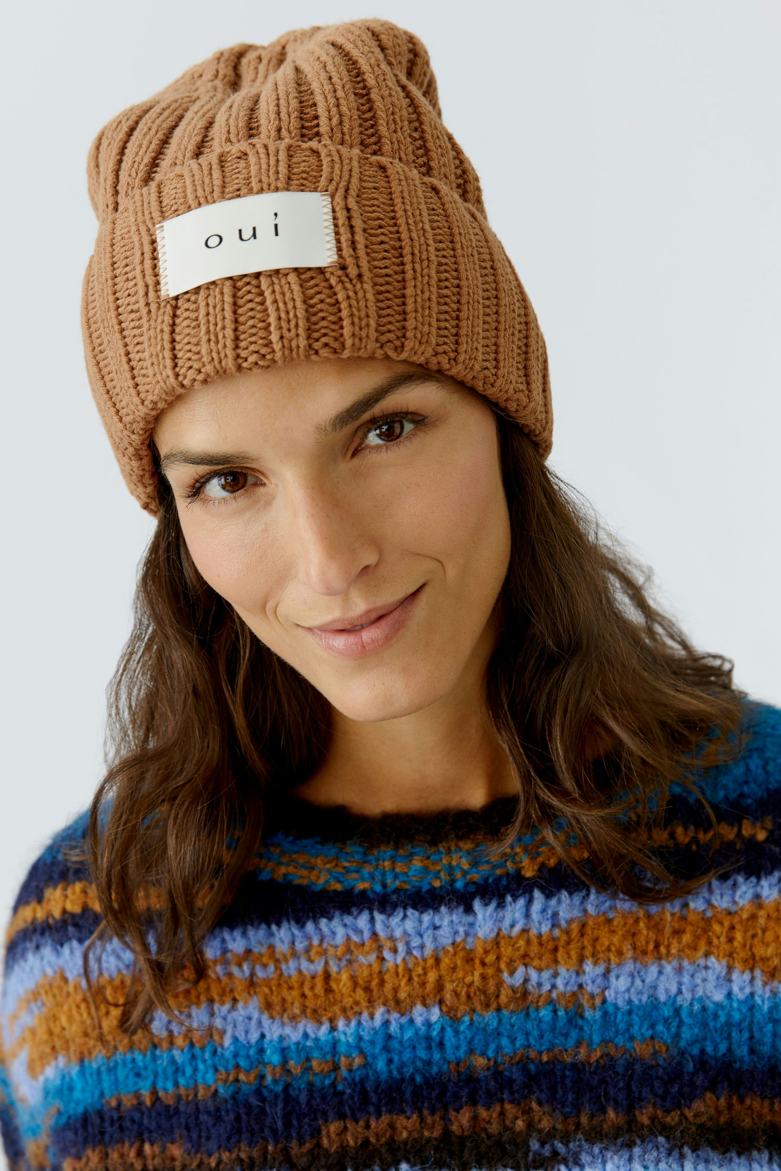 Cozy women's beanie: A woman wearing a brown ribbed knit hat with a logo patch.
